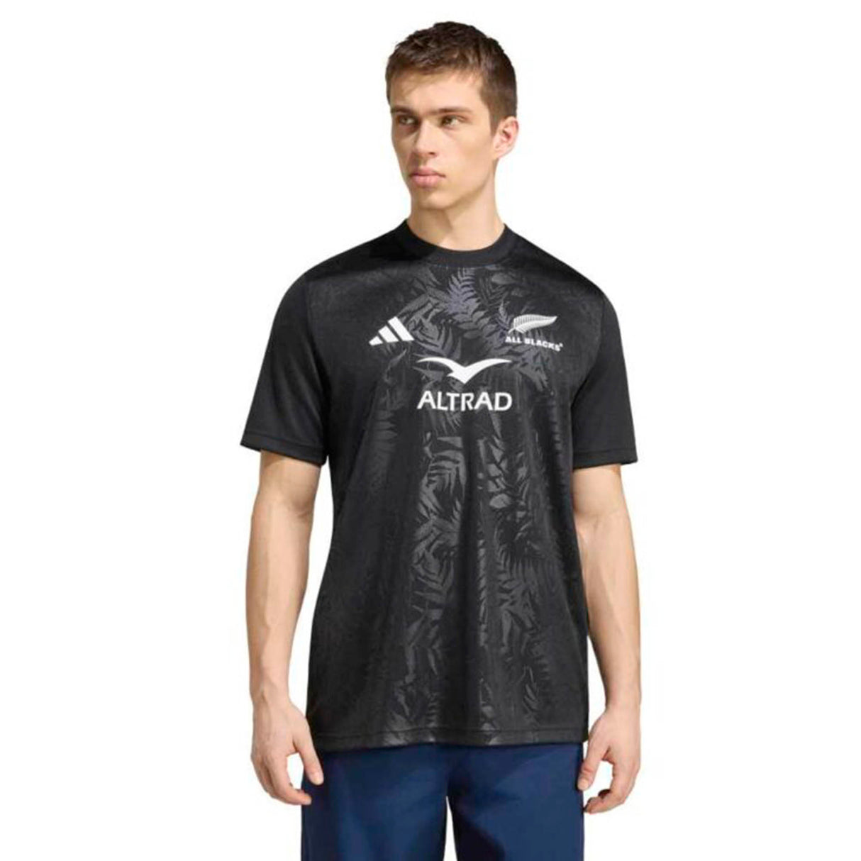 A man wearing the adidas All Blacks Greatest Rivalry Supporters Tee, featuring the adidas logo and representing New Zealand rugby, stands against a plain white background.