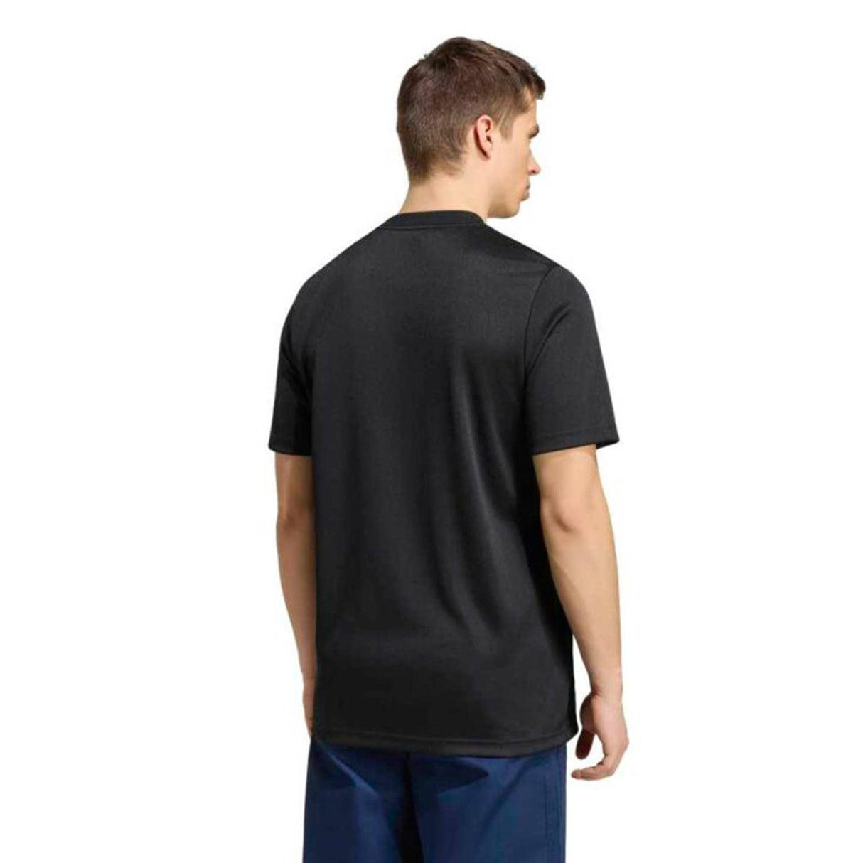 A person stands facing away from the camera, wearing an adidas All Blacks Greatest Rivalry Supporters Tee in black and blue pants against a white background.