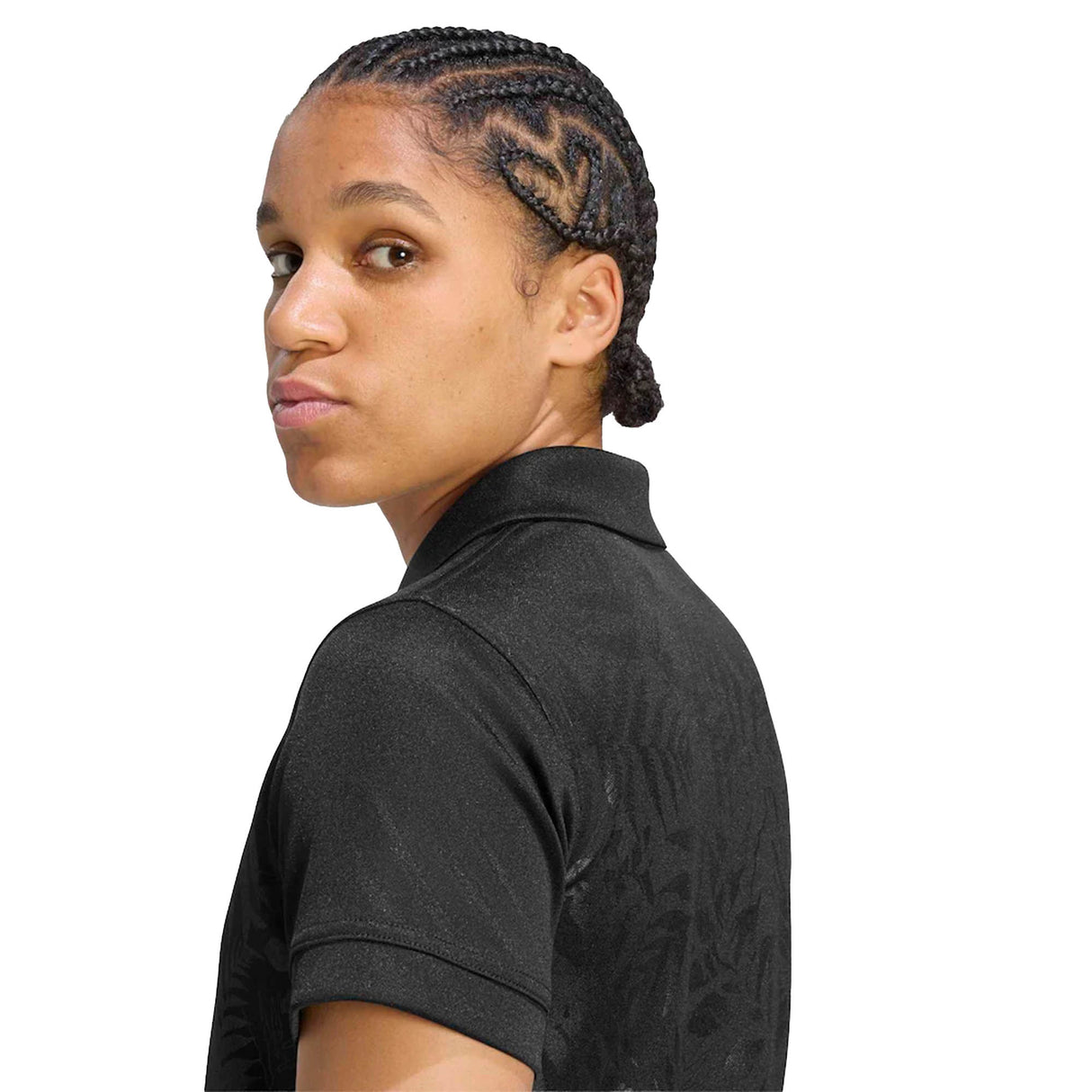 A person with braided hair wears the Women’s All Blacks Greatest Rivalry Replica Home Jersey by adidas, styled like an official team top, as they look over their shoulder against a white background.