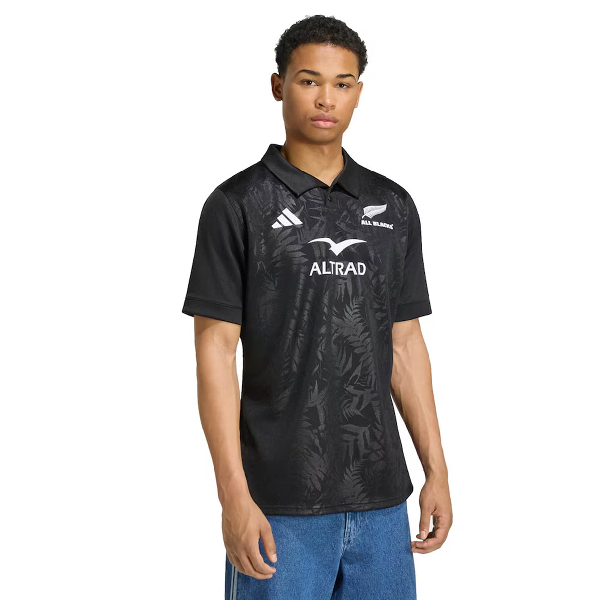 A young person wearing the adidas All Blacks Greatest Rivalry Replica Home Jersey, featuring adidas branding and a subtle leaf motif, stands against a plain background—honoring the storied rugby heritage of the team.