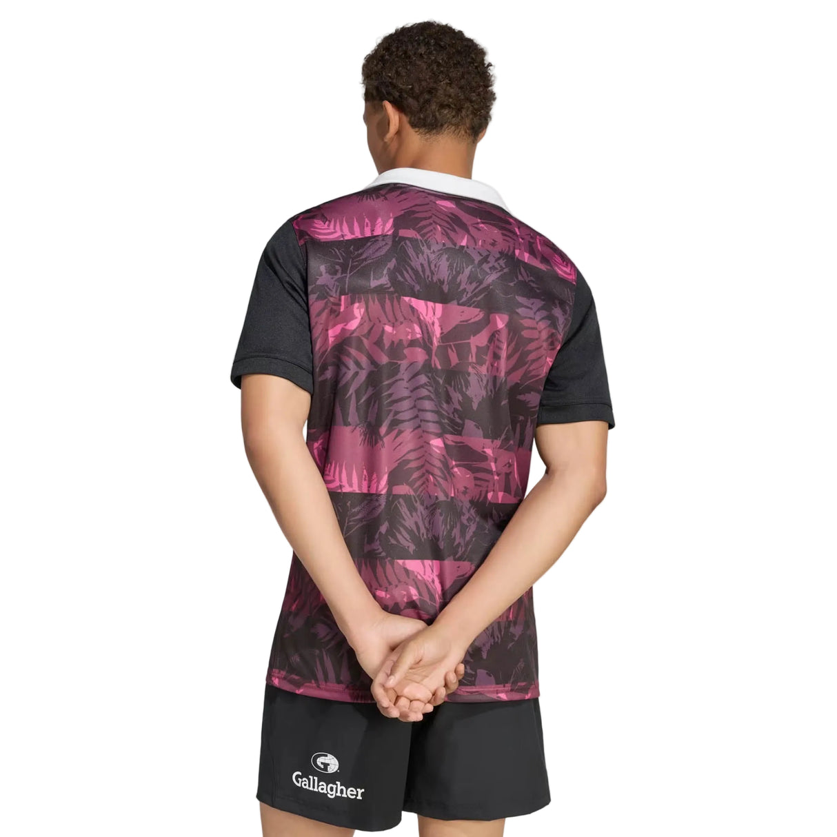 Wearing the adidas All Blacks 26/27 Training Jersey – South Africa Tour, which features a striking purple and black pattern, along with black shorts, a person stands hands behind their back and facing away, perhaps getting ready for the upcoming tour in South Africa.