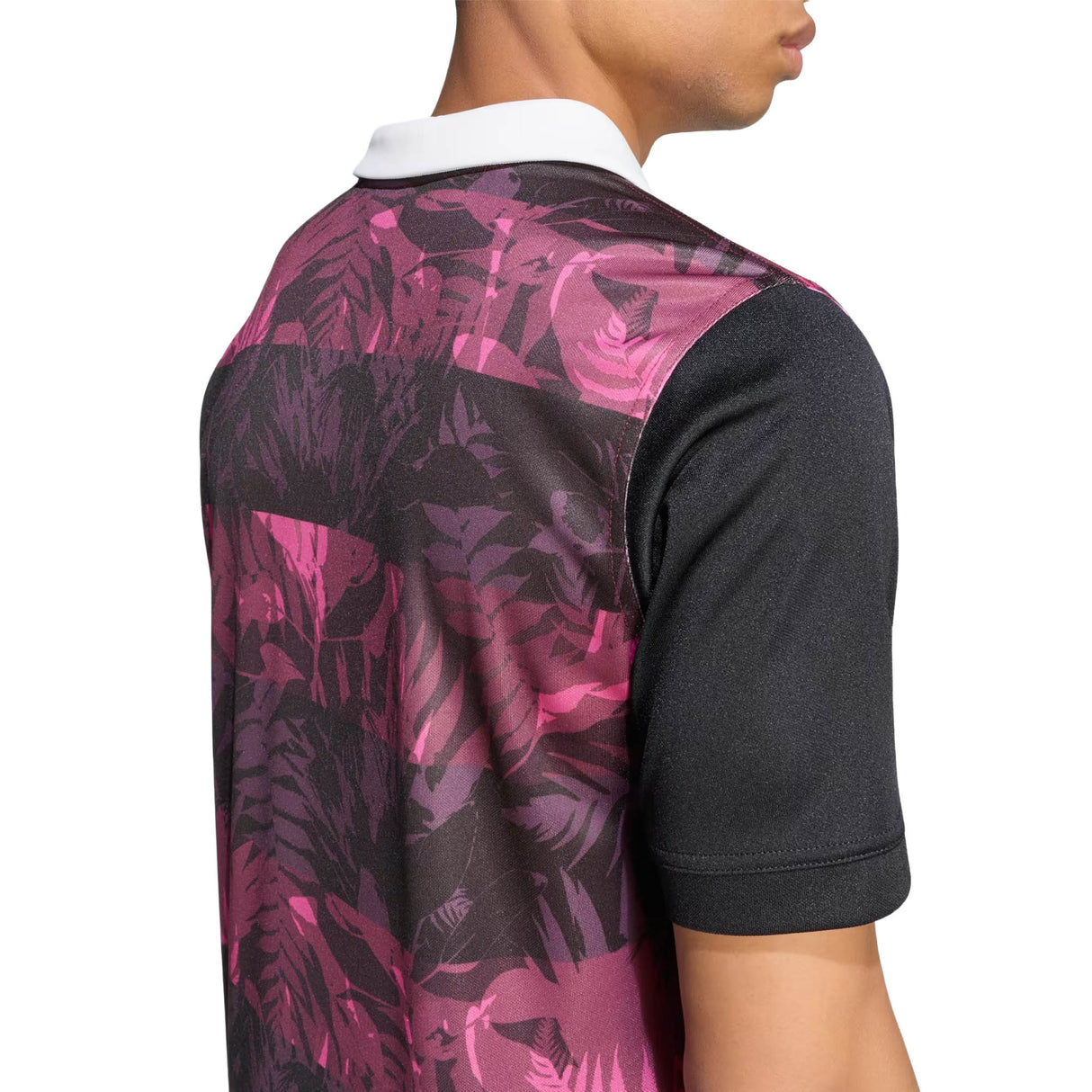 Person wearing the adidas All Blacks 26/27 Training Jersey – South Africa Tour, featuring a short-sleeve design with a pink and black tropical leaf pattern and a white collar, shown from the back and side.