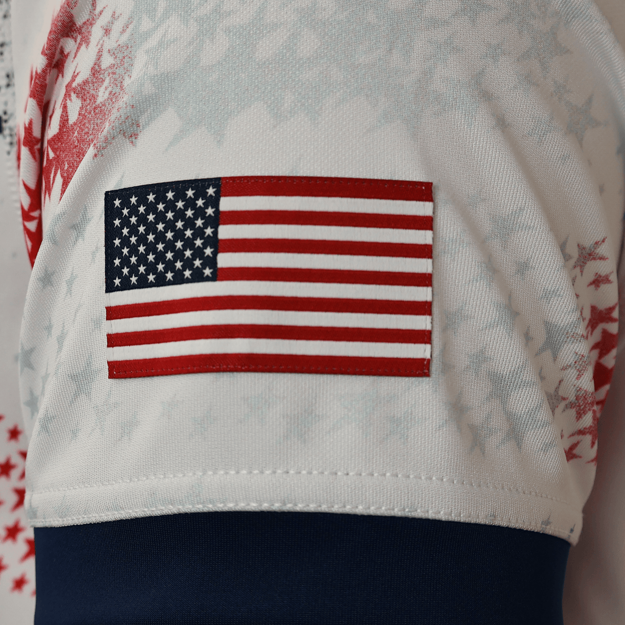 Close-up of the American flag patch on the USA Rugby 25/26 Home Replica Jersey by Macron, featuring faint star patterns and a dark blue band at the bottom.