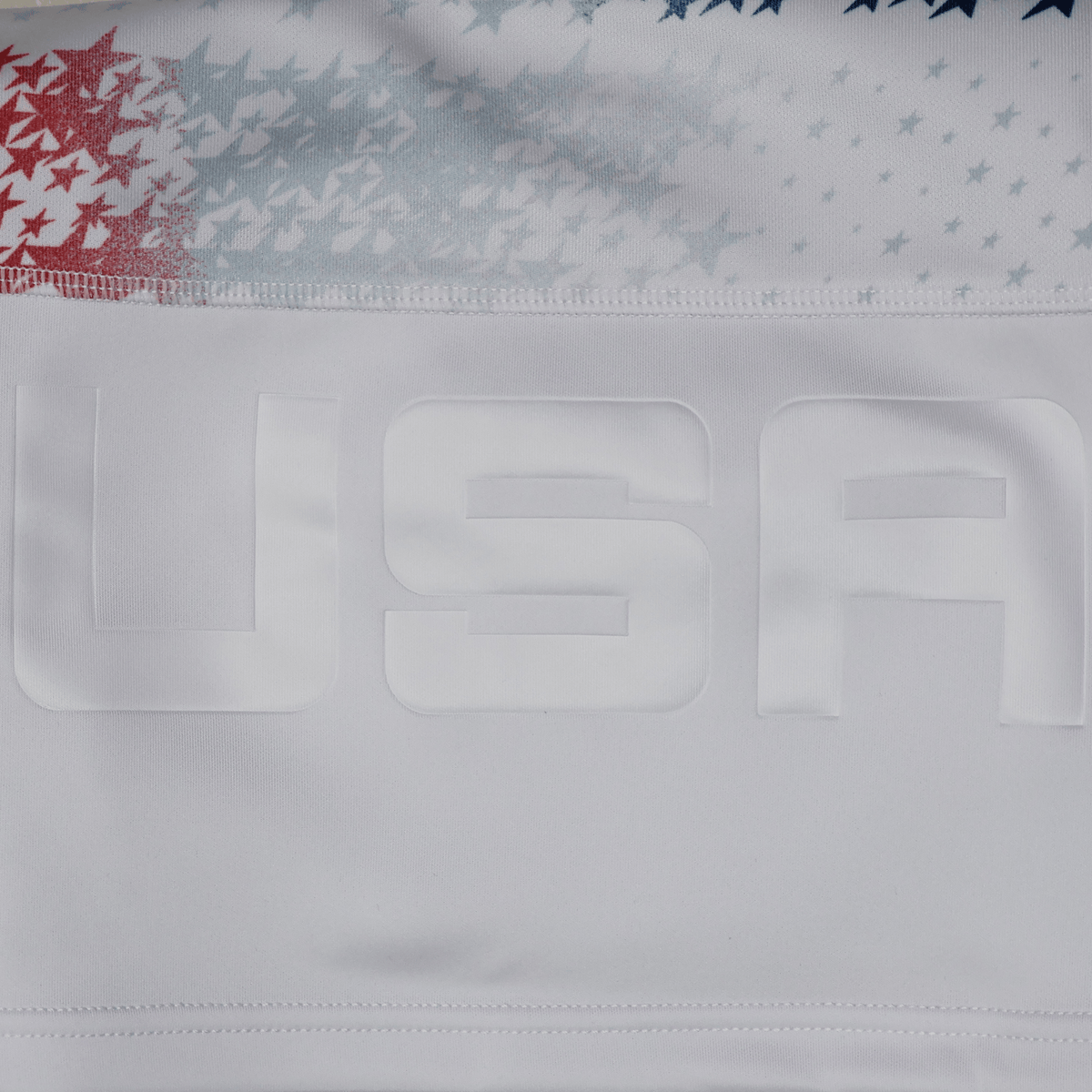 Close-up of the Women's USA Rugby M25/26 Home Replica Jersey by Macron, featuring "USA" in raised letters and a background of red, white, and blue stars.