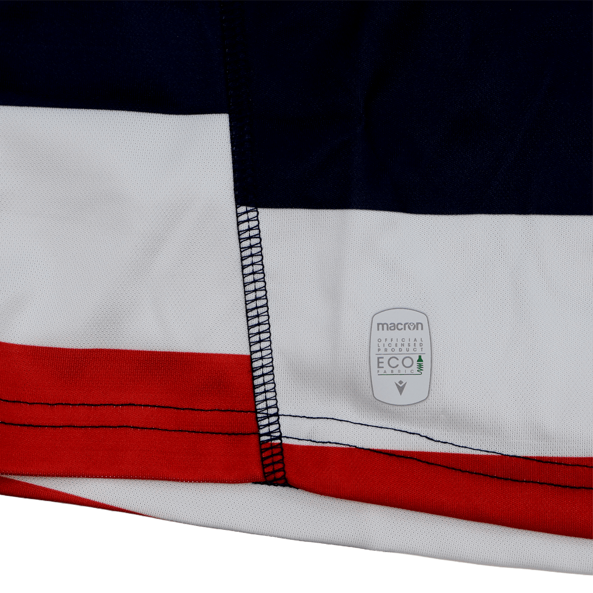 Close-up of the New England Free Jacks MLR 25/26 Replica Home Jersey by Macron, showing red, white, and dark blue striped fabric, visible stitching, and a small "macron eco" label.