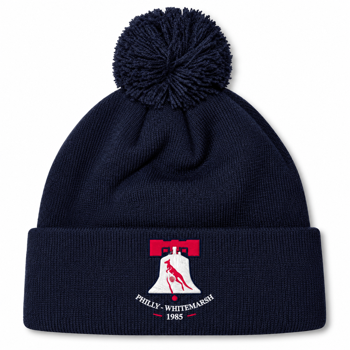 Navy blue pom-pom Philly Whitemarsh RFC Pom Pom Beanie by Canterbury with a cuff featuring an embroidered Liberty Bell icon, a kangaroo silhouette, and the text “Philly-Whitemarsh 1985.”.