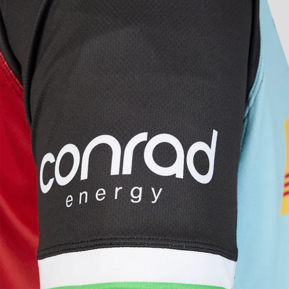 Close-up of a men’s home shirt sleeve from the Harlequins 26/27 Replica Home Jersey by Castore, featuring the text “conrad energy” printed in white on a black background.