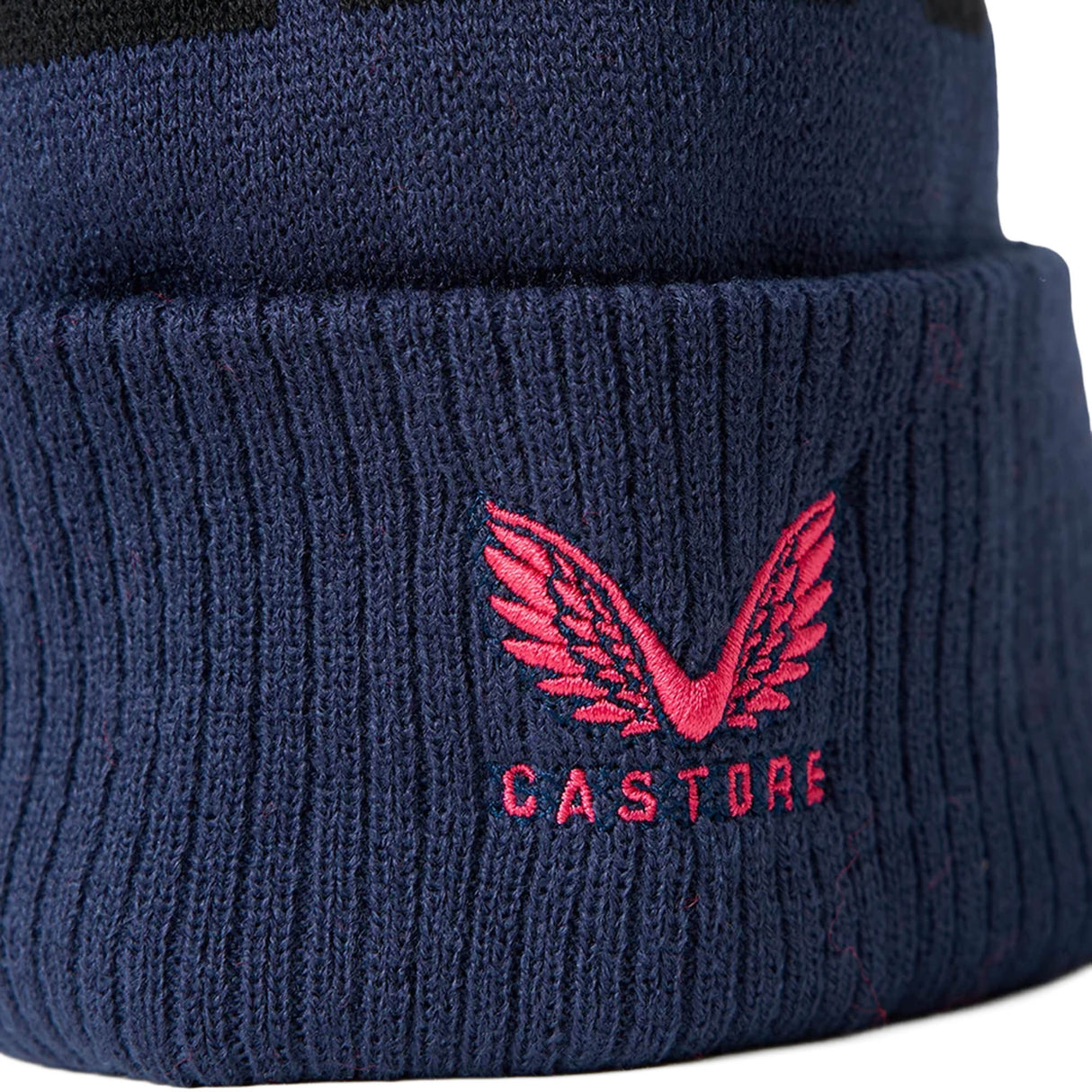Close-up of the England 26/27 Bobble Beanie by Castore, featuring a navy blue knit design with a pink embroidered wing logo and “CASTORE” lettering on the cuff—perfect for any dedicated England rugby fan.