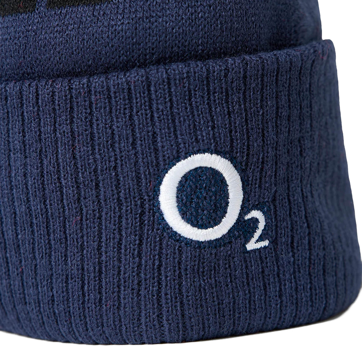 Close-up of the England 26/27 Bobble Beanie by Castore, a navy blue ribbed knit hat with a white embroidered “O₂” logo on the cuff—making it the perfect choice for any dedicated England rugby supporter throughout the winter season.