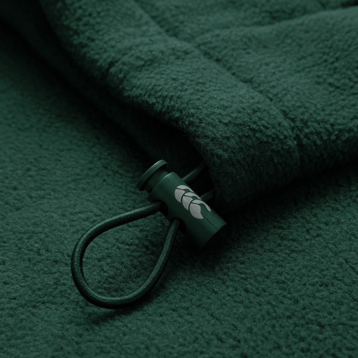 Close-up of the Ireland 26 Retro Fleece 1/4 Zip by Canterbury, showcasing its dark green fleece fabric, cord with a plastic toggle adorned with a small white leaf design—evoking the classic style of vintage Canterbury training pullovers.