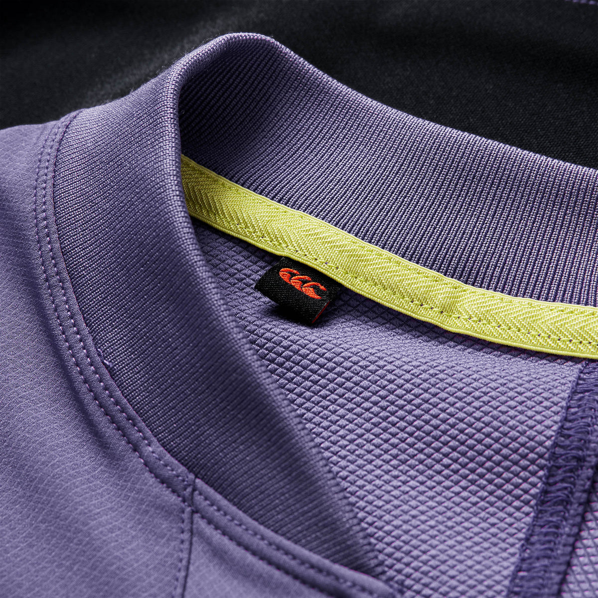 Close-up of the collar on the Ireland 26 Tech Drill Top by Canterbury, highlighting the purple fabric with yellow inner trim and a black tag featuring a red logo—premium details that exemplify official Canterbury IRFU training wear.