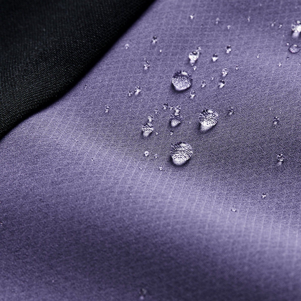 Close-up of water droplets on the purple Ireland 26 Tech Drill Top by Canterbury, with a black fabric corner, highlighting the water resistance and quality craftsmanship of Canterbury IRFU training wear.