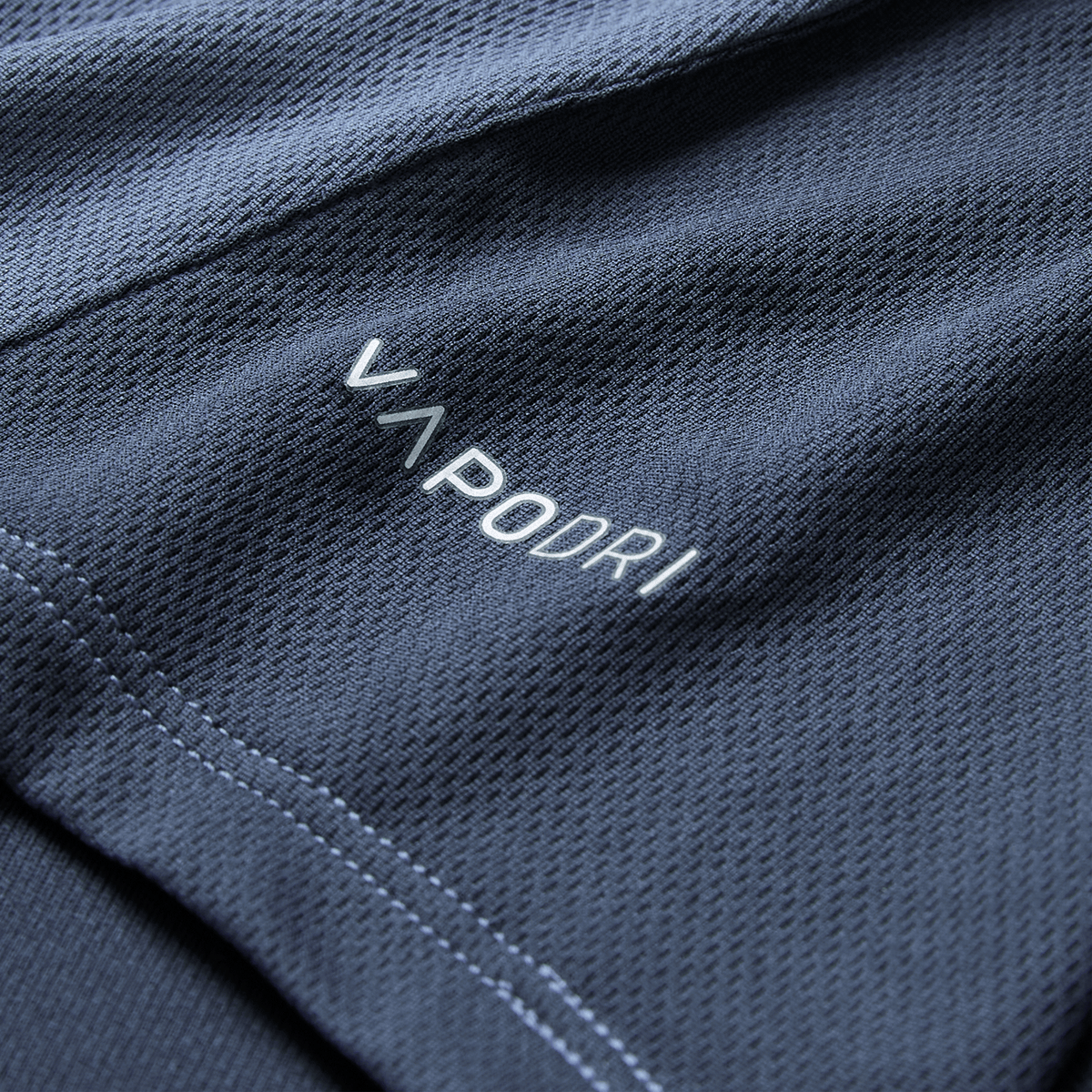 Close-up of dark blue textured fabric from the Ireland 26/27 Summer Tour Superlight Training Singlet by Canterbury, featuring "VAPODRI" in white and light blue stitching along the seam.