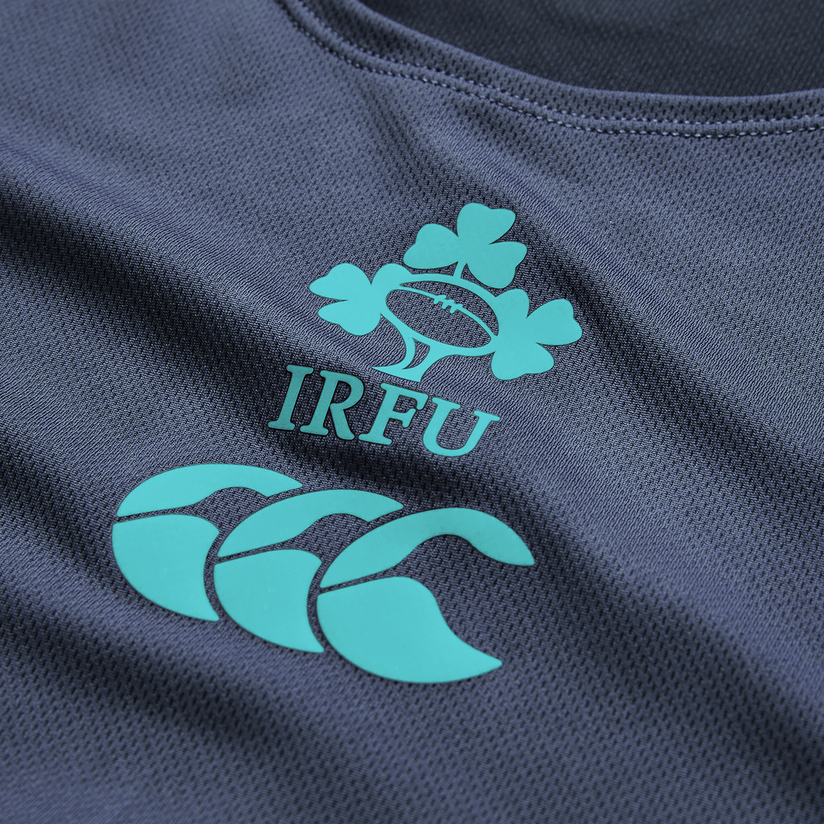 Close-up of the Ireland 26/27 Summer Tour Superlight Training Singlet by Canterbury, in dark blue, featuring the IRFU clover and Canterbury logos in teal—a lightweight design ideal for training.