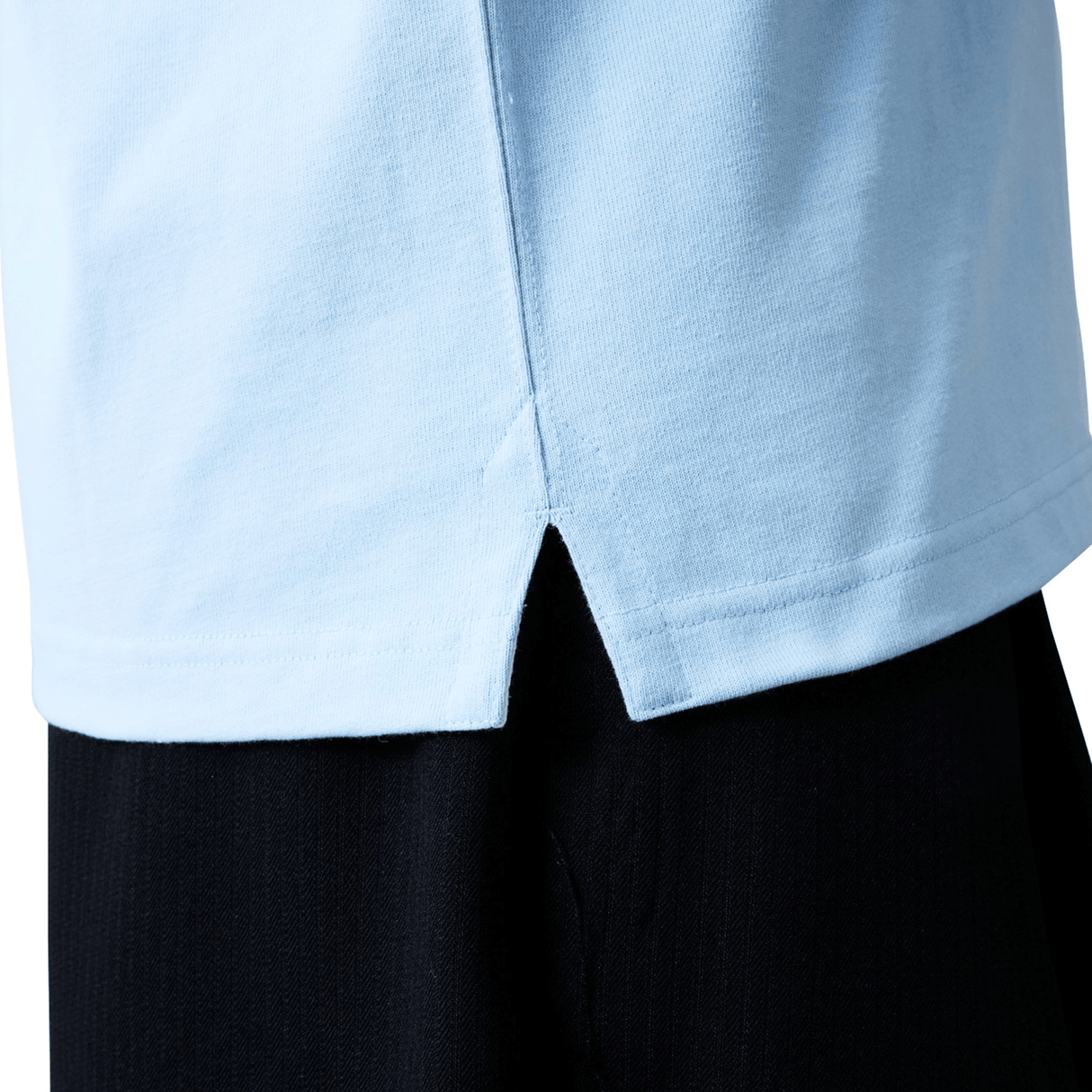 Close-up of the lower hem of the Canterbury Solid Dye Rugby Jersey by Canterbury in light blue, featuring a center split, worn over black pants.
