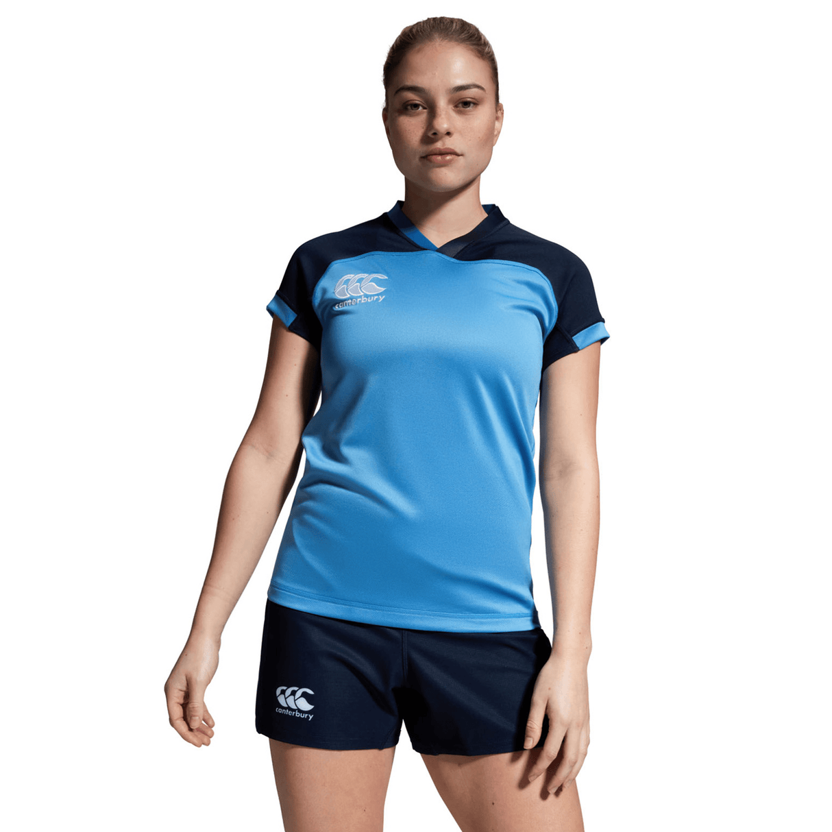 A person poses against a plain white background, wearing a blue sports jersey and navy Women's Canterbury Yokohama Shorts, both displaying the Canterbury logo. The Vapodri fabric offers advanced comfort.