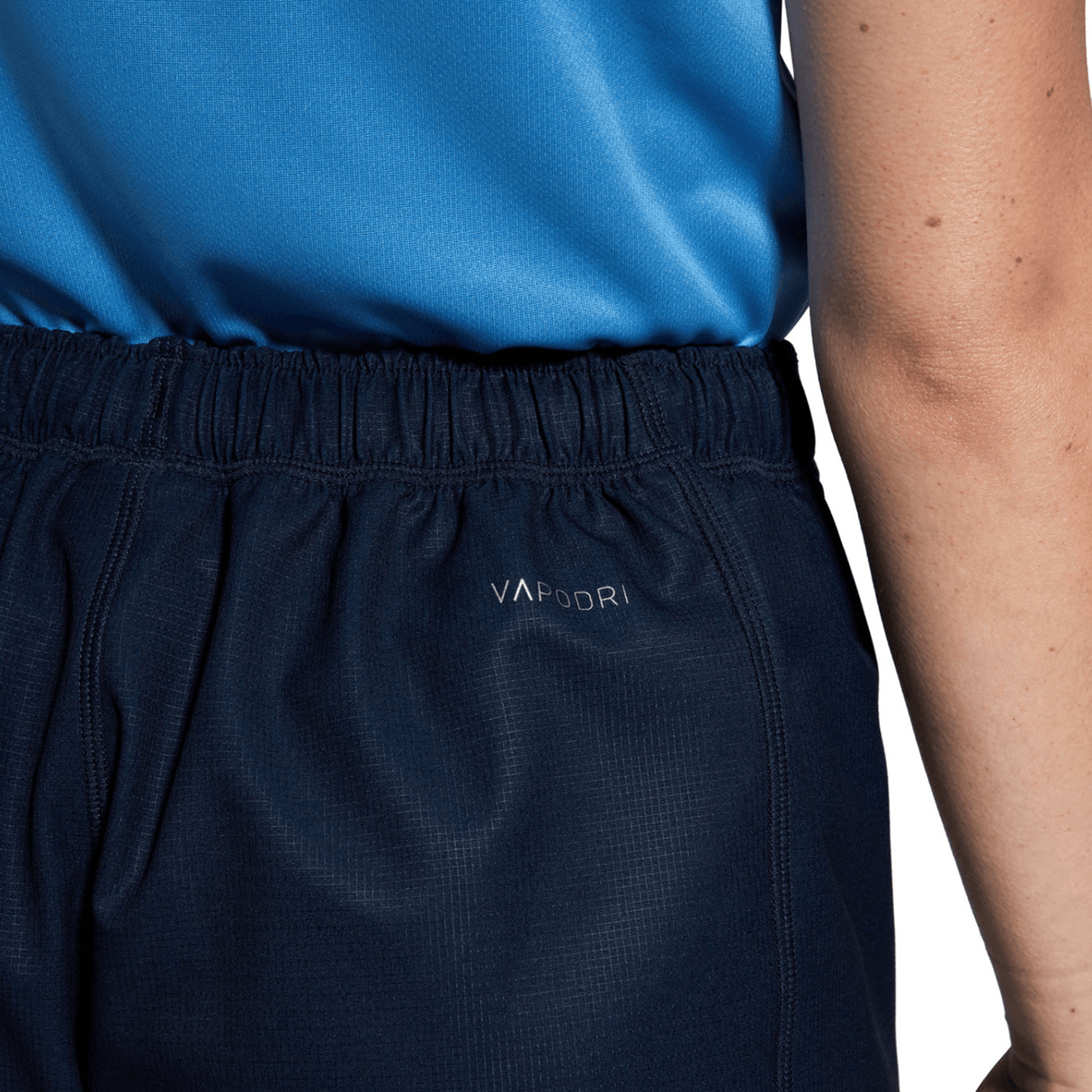 A person is seen from the back wearing the Women's Canterbury Yokohama Short, featuring dark athletic shorts and a blue shirt with "VaporDri" branding and the Canterbury logo.