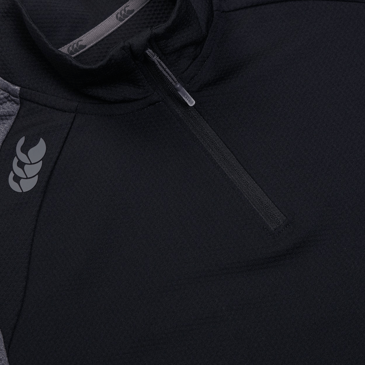 Close-up of a black Canterbury Women's Elite First Layer quarter-zip jacket, featuring VapoDri technology, a subtle shoulder logo, and an intricate honeycomb pattern.