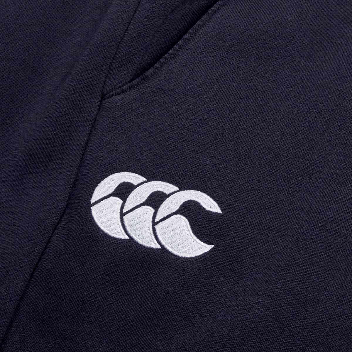 Close-up of a dark fabric with a white Canterbury logo featuring three overlapping curved shapes, crafted from cotton blend fleece on Women's Leisure Sweatpants by Canterbury.