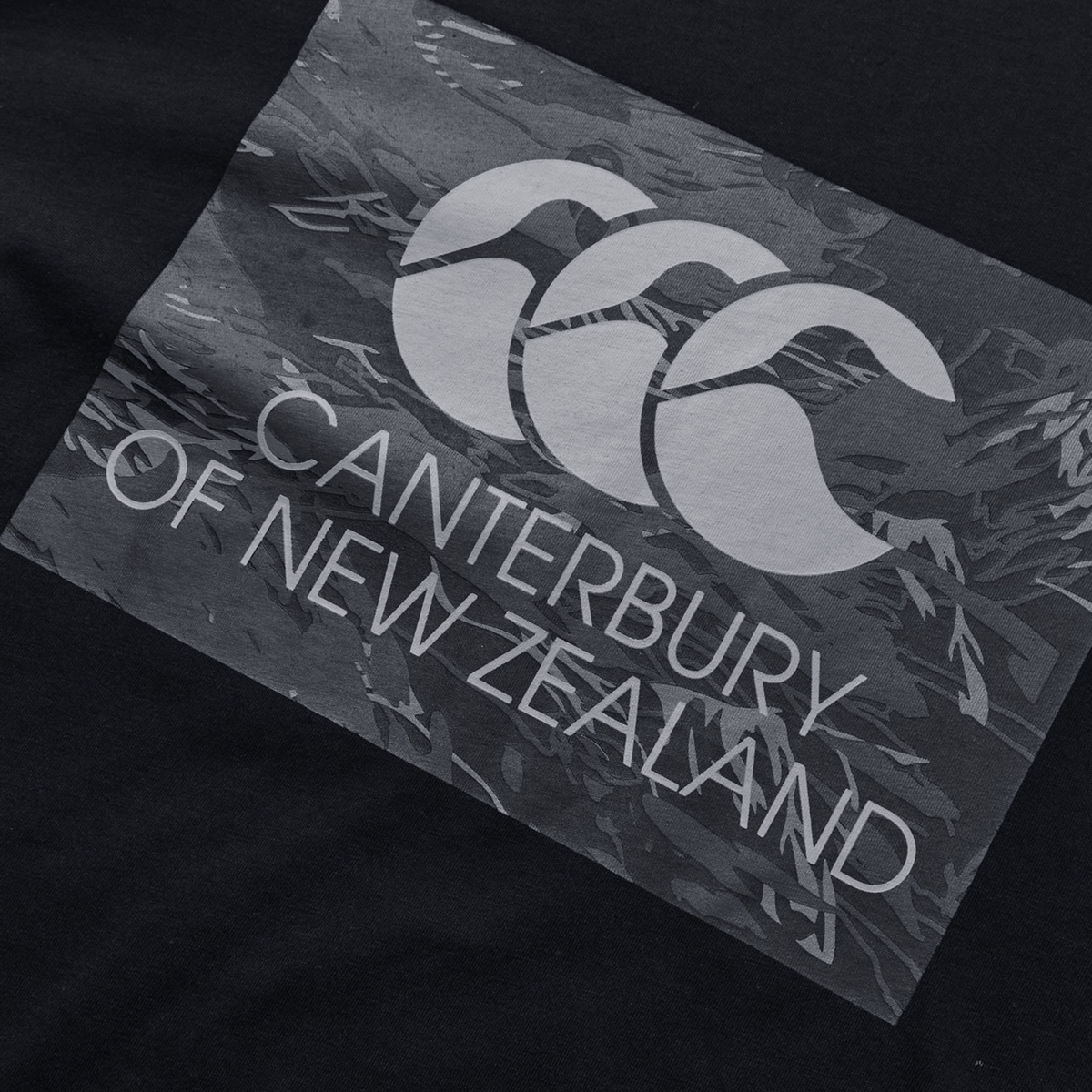 The image displays a relaxed-fit Canterbury Force T-Shirt by Canterbury, featuring a black fabric with a gray graphic of three overlapping C's and the text "Canterbury of New Zealand," making it ideal for various casual occasions.