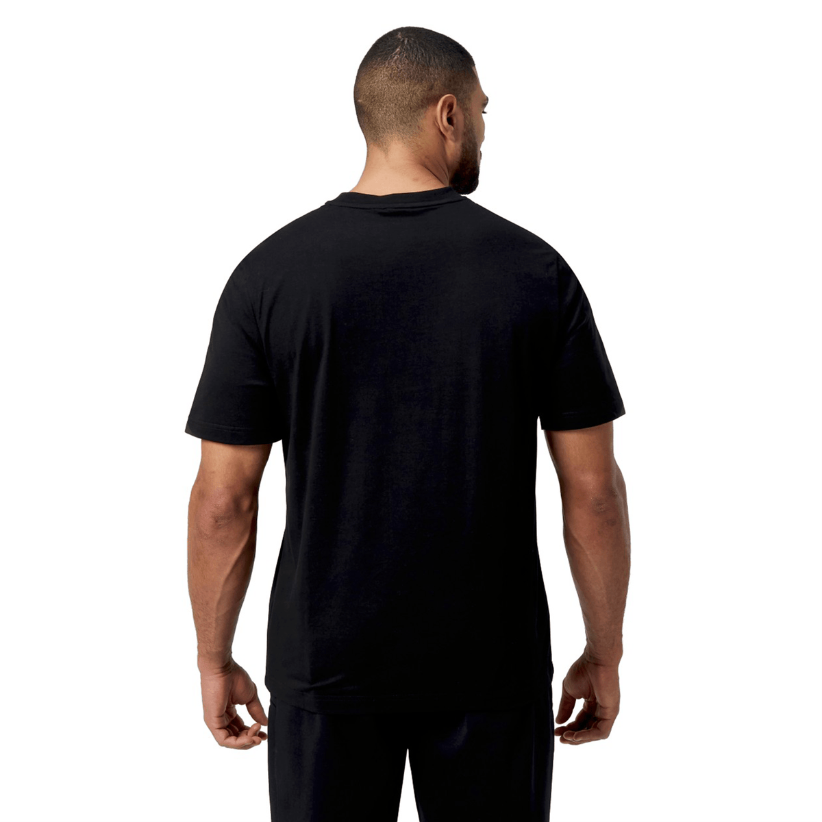 Against a white background, an individual faces away from the camera, highlighting the versatility and relaxed fit of a Canterbury Force T-Shirt and black pants.