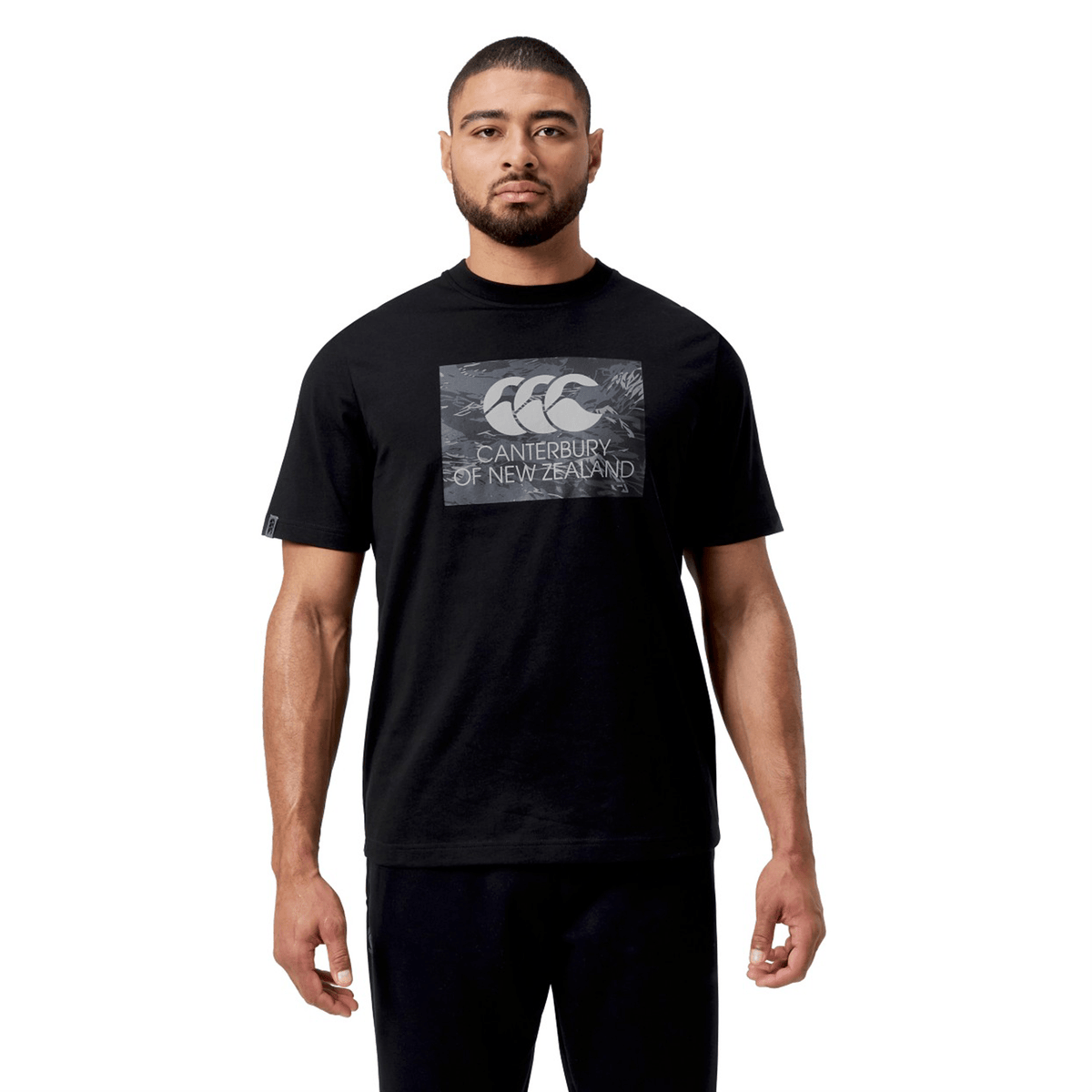 A man in a black Canterbury Force T-Shirt and pants stands against a white backdrop, effortlessly highlighting the versatility and relaxed fit of the outfit.