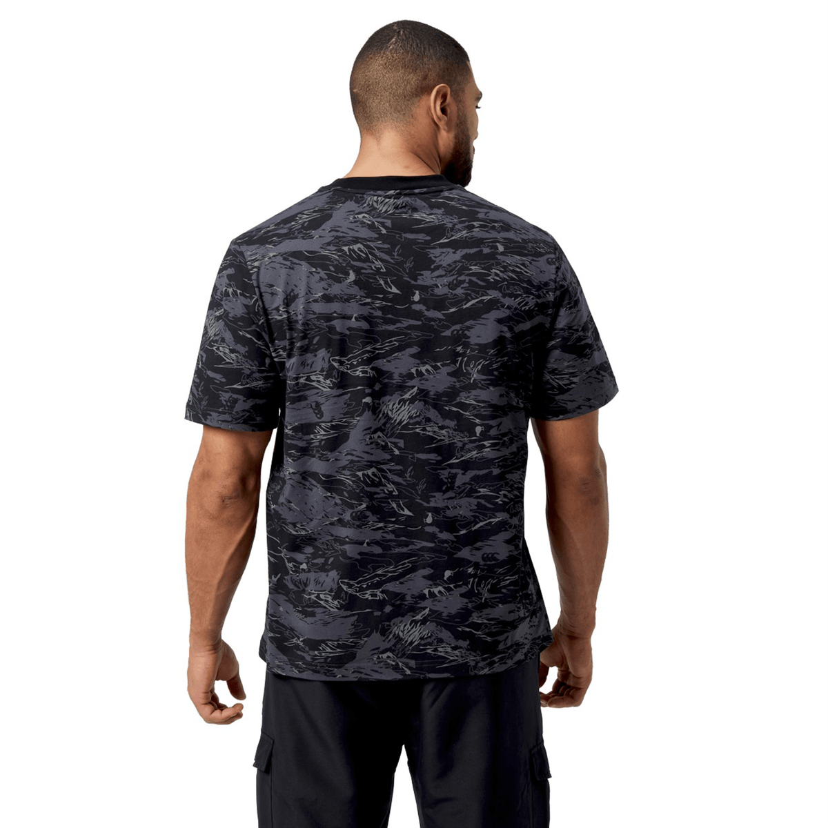 A man wearing a Canterbury Force AOP T-Shirt with CCC camouflage print and black shorts stands with his back to the camera.