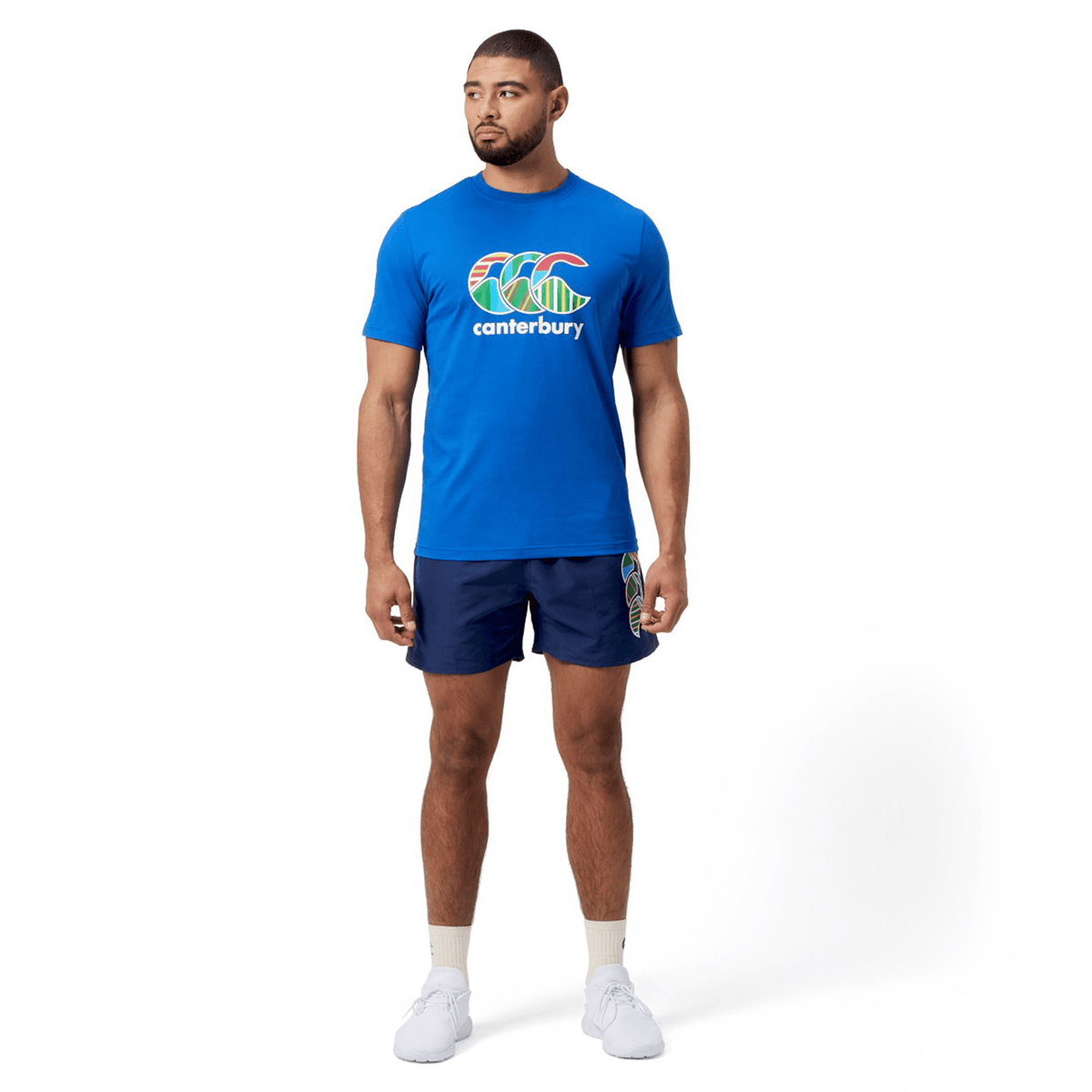 A man is standing in a Canterbury Uglies T-Shirt, paired with navy shorts and white sneakers.