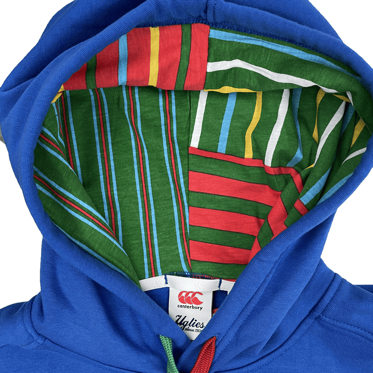 The Canterbury Uglies Hoodie has a blue exterior with bold block colors inside the hood's multicolored striped lining. A white "Canterbury" label at the hood's base and a stylized CCC logo enhance its vibrant look.