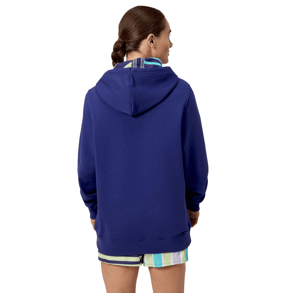 A person in a blue Canterbury Women's Uglies Hoodie and striped shorts, facing away. Their hair is tied back in a braid, highlighting the relaxed fit of this women's cut garment from Canterbury.