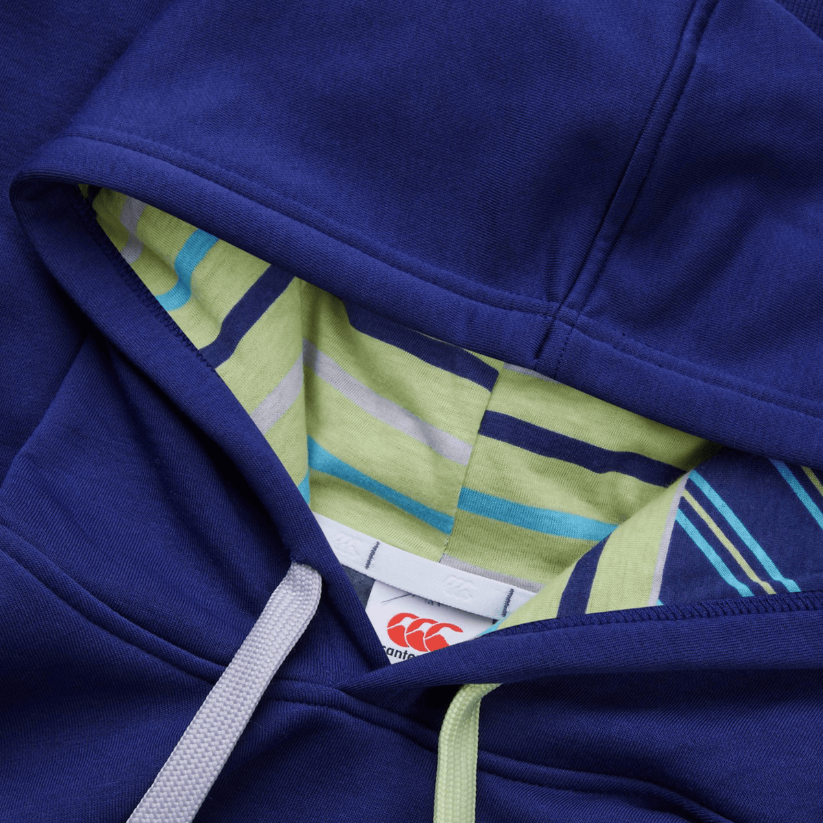 Close-up of a Canterbury Women's Uglies Hoodie featuring a blue design, striped inner lining, and white drawstrings with the tag displaying the red Canterbury logo inside the hood.
