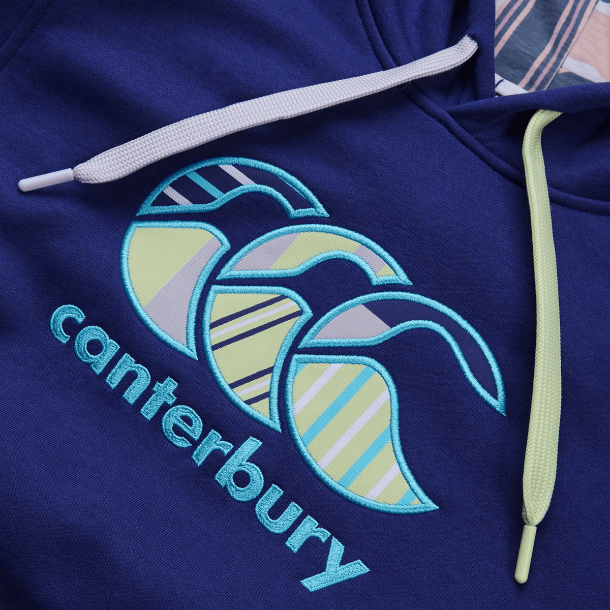 The Canterbury Women's Uglies Hoodie features "Canterbury" in blue with vibrant yellow and blue abstract shapes and striped patterns. Light-colored drawstrings elegantly hang above the logo, enhancing its stylish appeal.