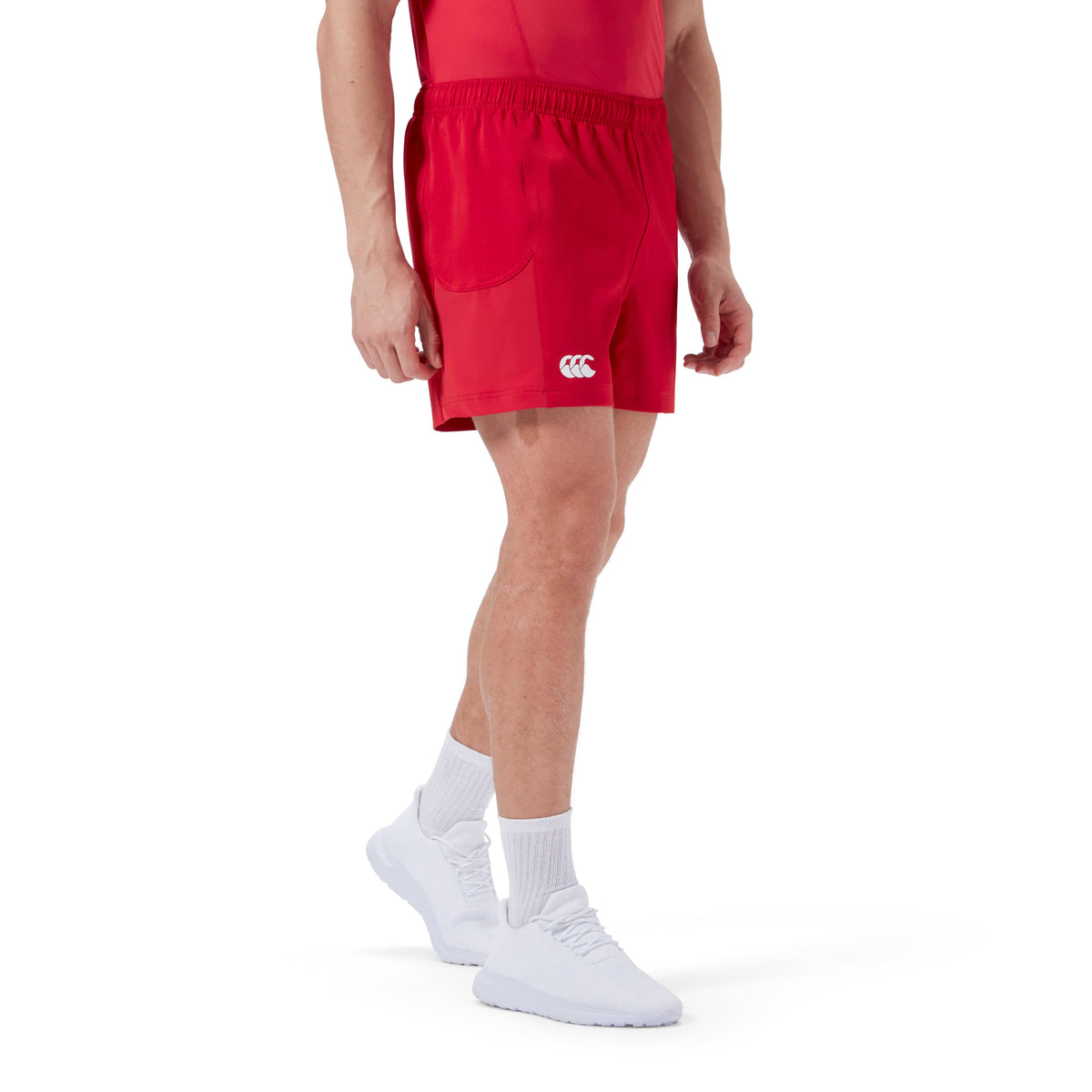 A person wearing red Canterbury Advantage Short 2.0 athletic shorts, a red top, white socks, and white sneakers is shown against a plain white background.