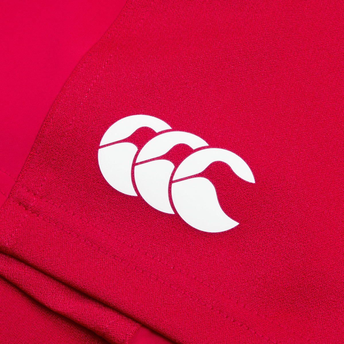 The Women's Canterbury Advantage Short 2.0 showcases a close-up of a red fabric with a white Canterbury logo, featuring three overlapping curves, crafted from recycled content for sustainability and performance.