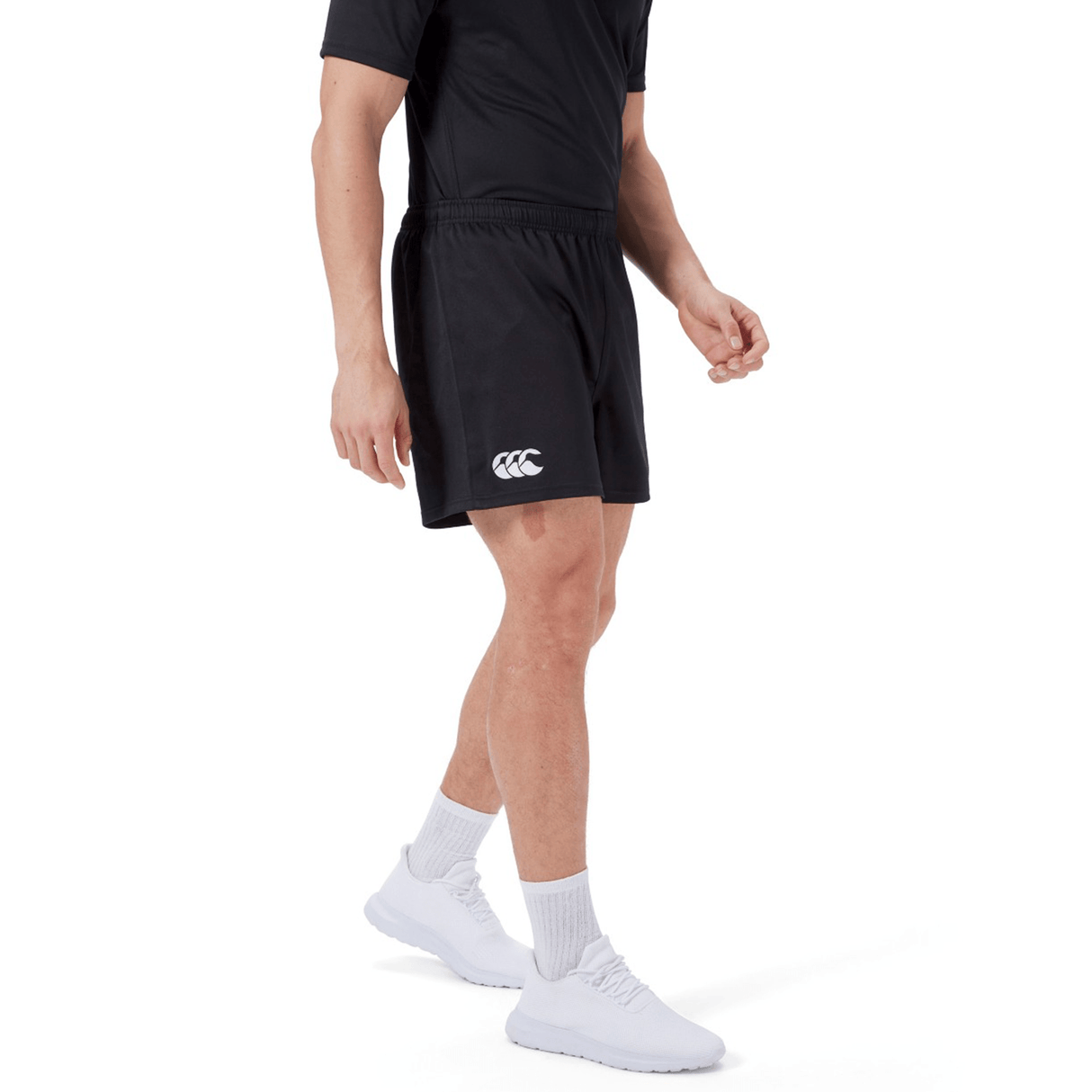 Someone is wearing Canterbury's black Professional Short 2.0, a black T-shirt, white socks, and white sneakers while standing against a plain background.