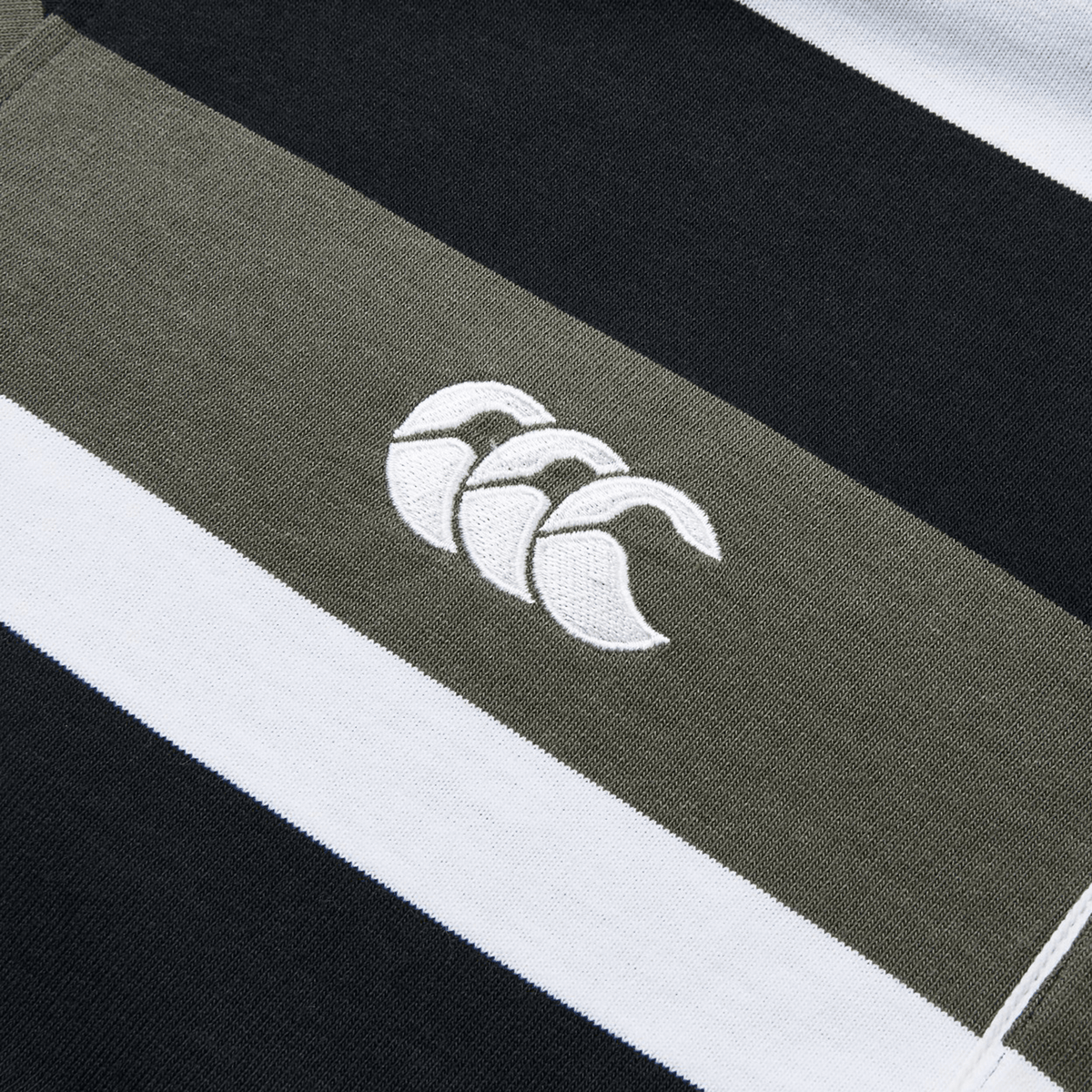 A close-up of the Canterbury Yarn Dye Long Sleeve Striped Rugby Jersey highlights its horizontal black, olive green, and white yarn-dyed stripes, with an embroidered logo of three overlapping curves.
