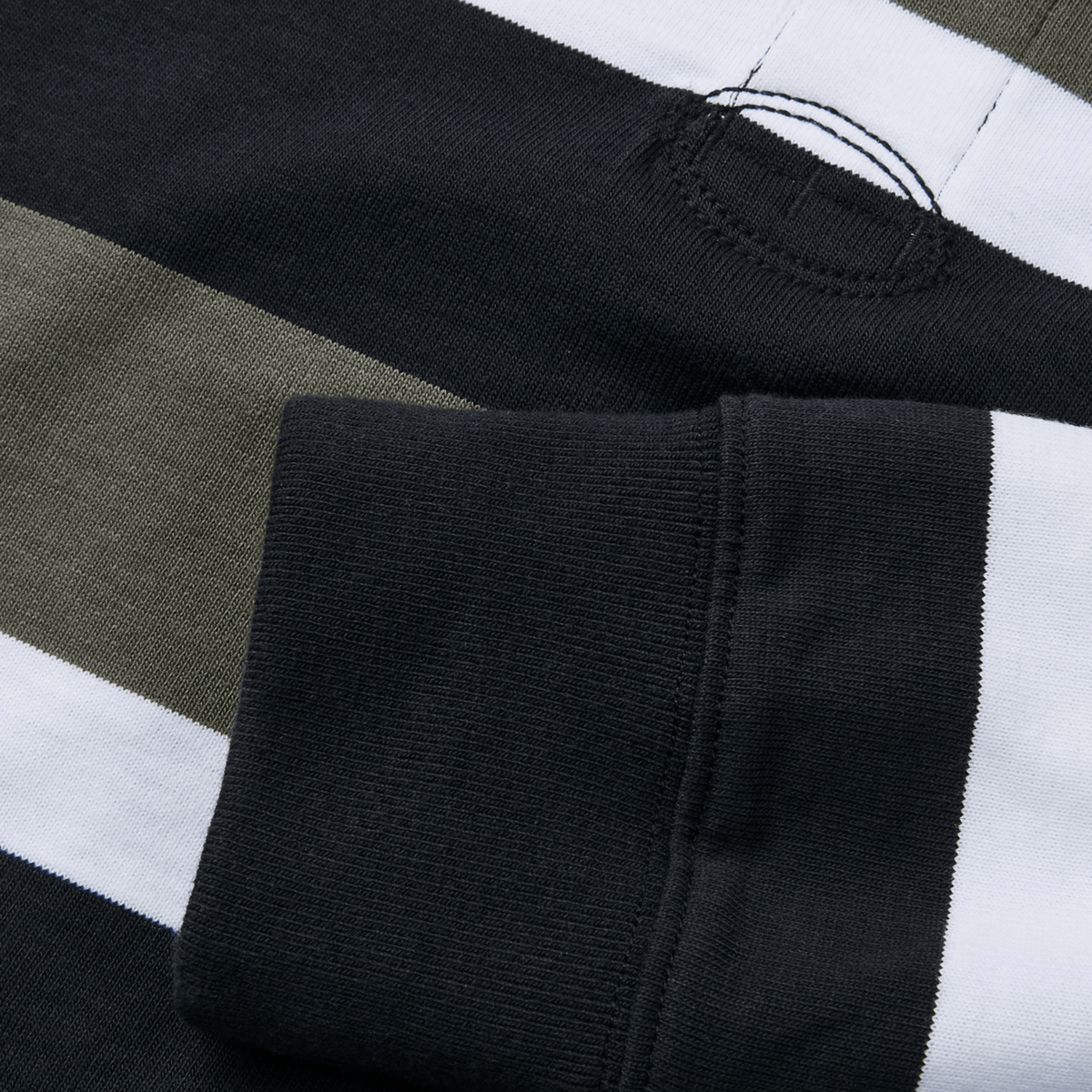 A close-up of the Canterbury Yarn Dye Long Sleeve Striped Rugby Jersey shows black, white, and olive stripes. The yarn-dyed fabric includes a stitched buttonhole at the top, and a rolled black cuff is visible at the bottom.