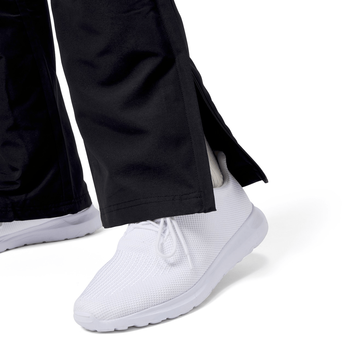 A close-up features a person in Canterbury's Force Straight Leg Pant, highlighting ankle zips over white sneakers. The unzipped straight leg design stylishly reveals the shoe's heel and ankle, merging fashion with activewear functionality.