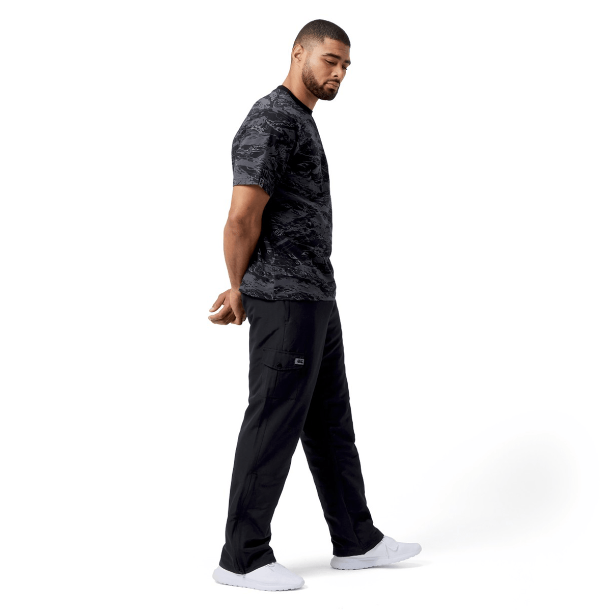 A man in a black camo t-shirt and Canterbury Force Straight Leg Pant stands against a white background, facing left with his hands clasped behind his back.