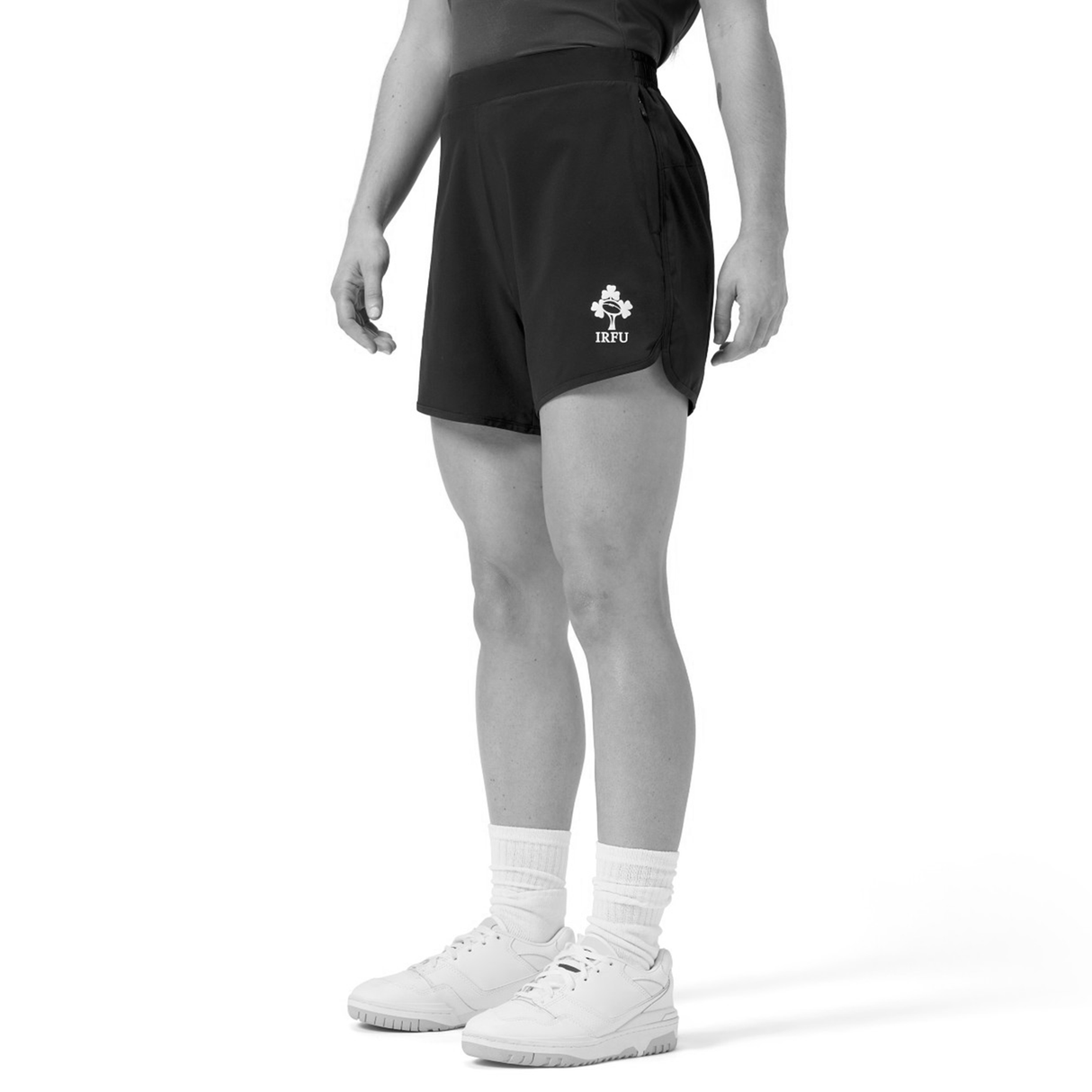 A woman wears Canterbury Women’s Ireland 25/26 Woven Gym Shorts, paired with white socks and sneakers, standing against a plain white background.