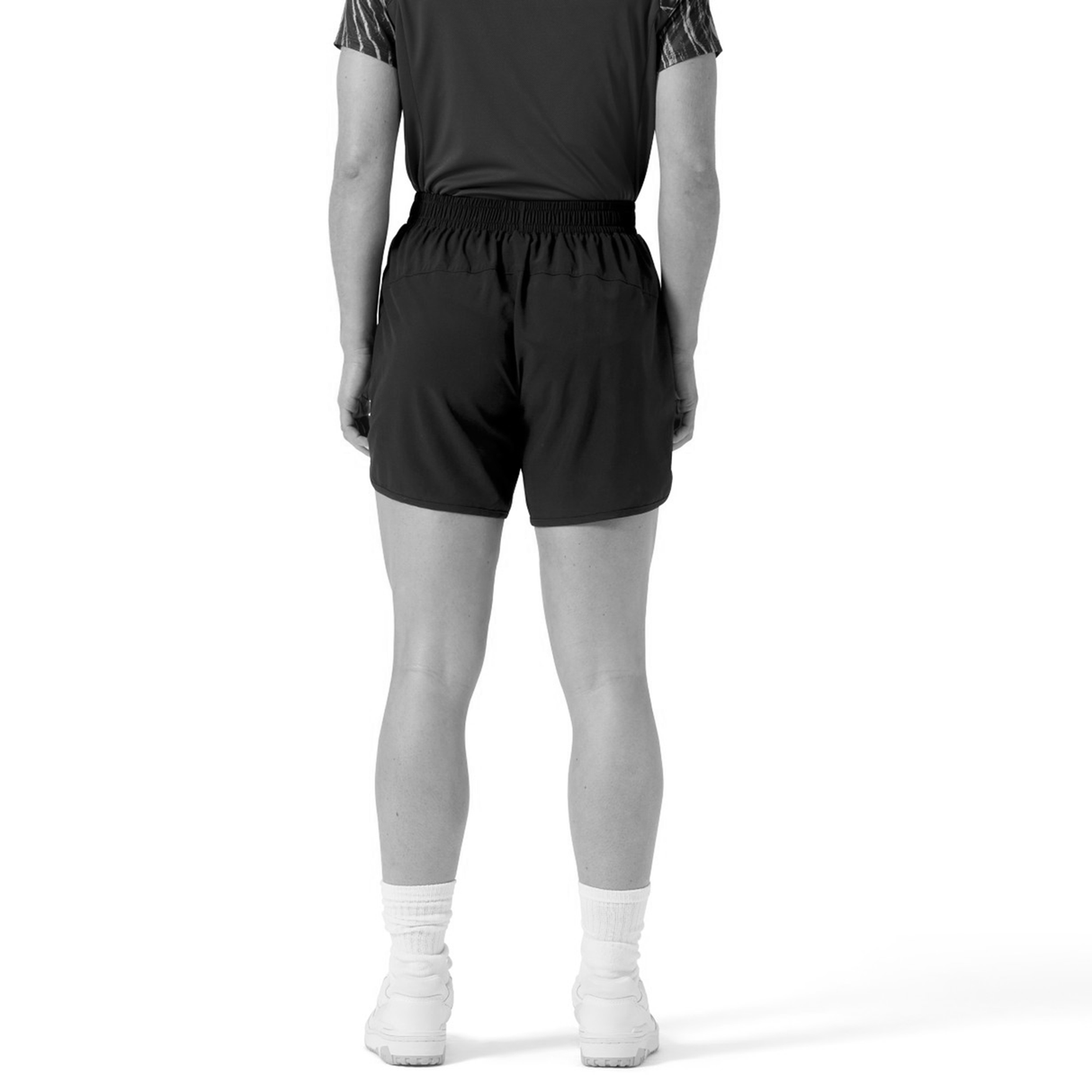 A person faces away from the camera, wearing a short-sleeve shirt, socks, sneakers, and Canterbury Women's Ireland 25/26 Woven Gym Short, with a plain white background.