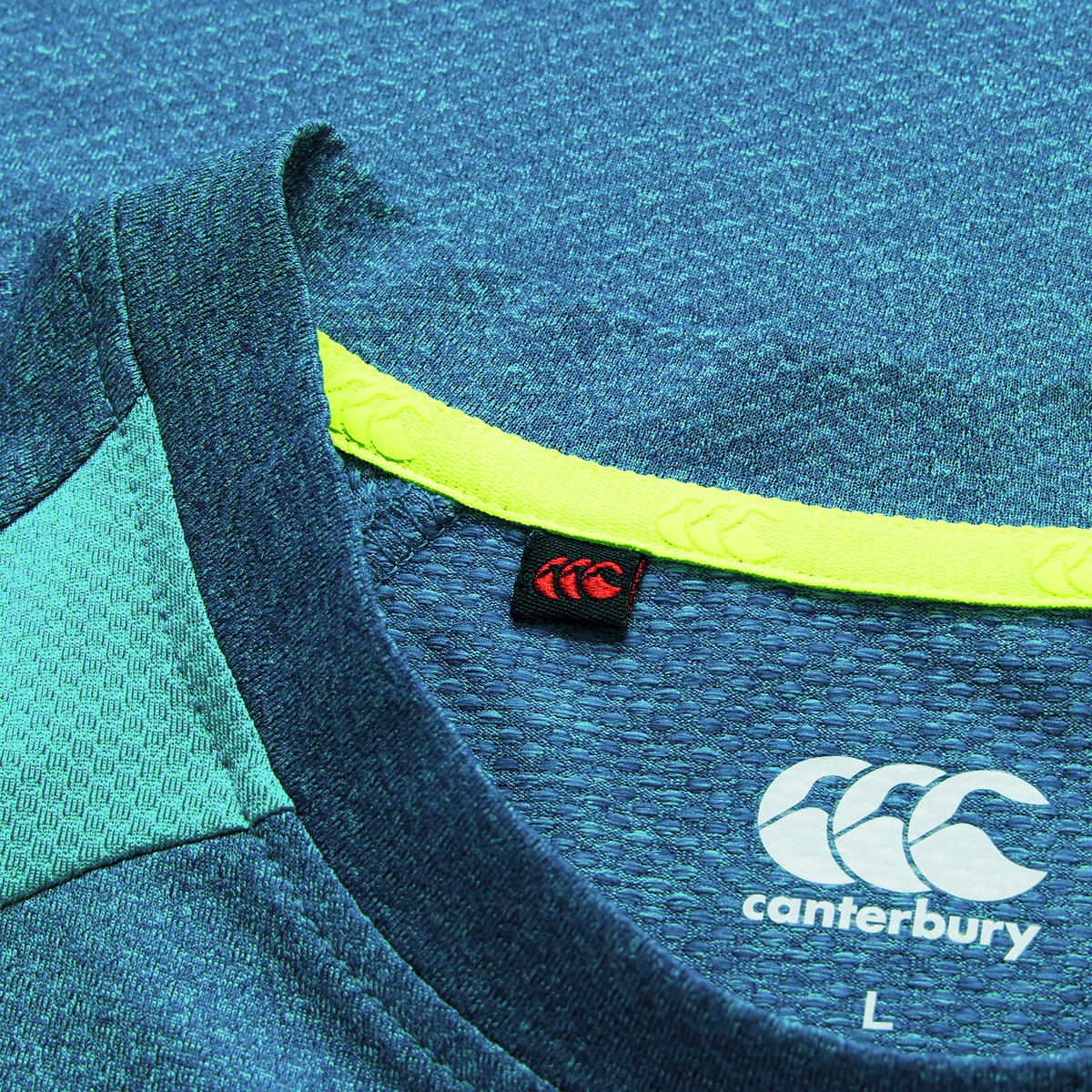 Close-up of the Ireland 26/27 Summer Tour Elite Training Tee by Canterbury in blue, featuring collar detail, neon yellow trim, red tag, and Canterbury logo with size "L"—a top choice rugby performance shirt.