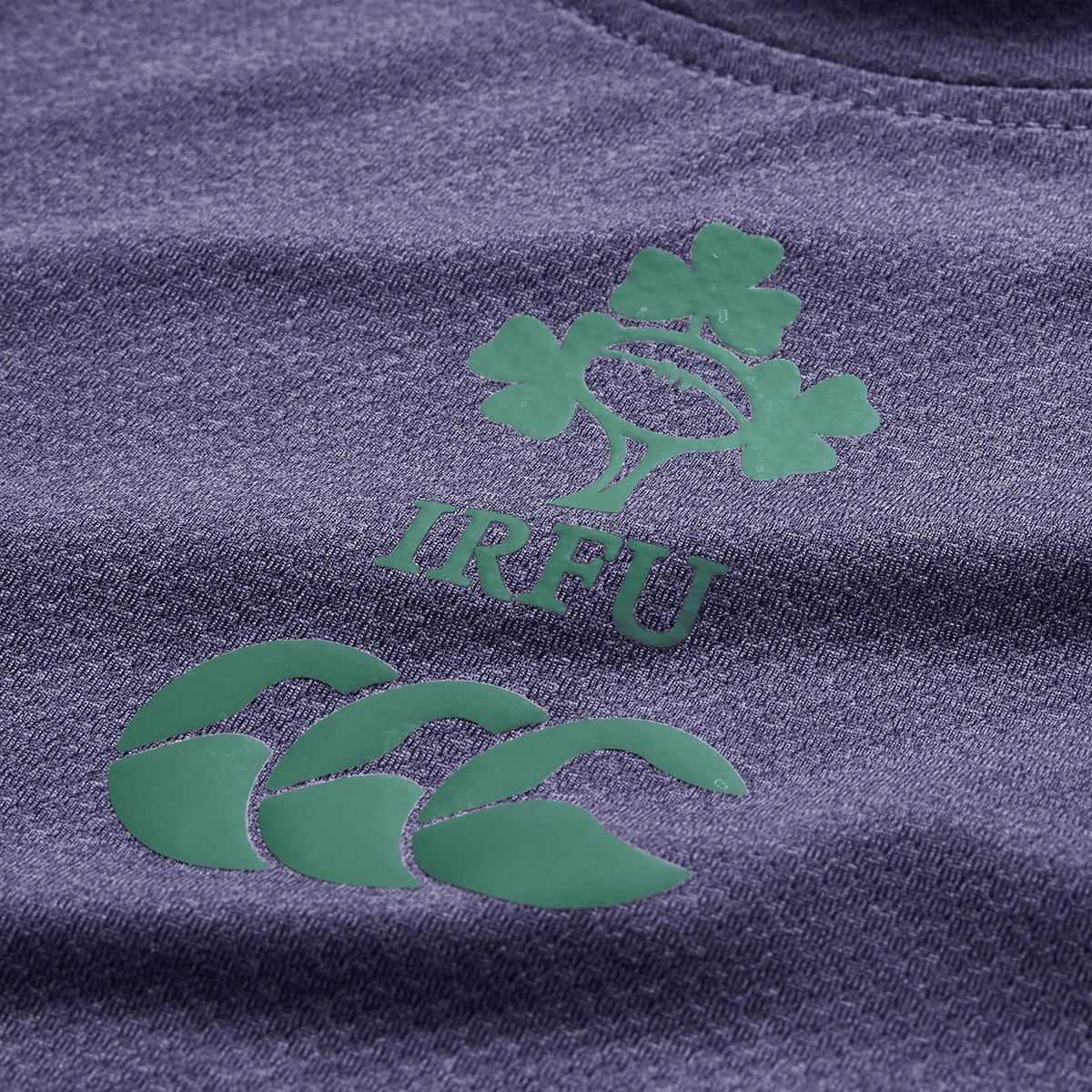 Close-up of a textured purple fabric featuring the IRFU clover rugby logo and the green CCC logo, highlighting Vapodri breathable sportswear technology as seen in the Ireland 26 Elite Training Tee by Canterbury.