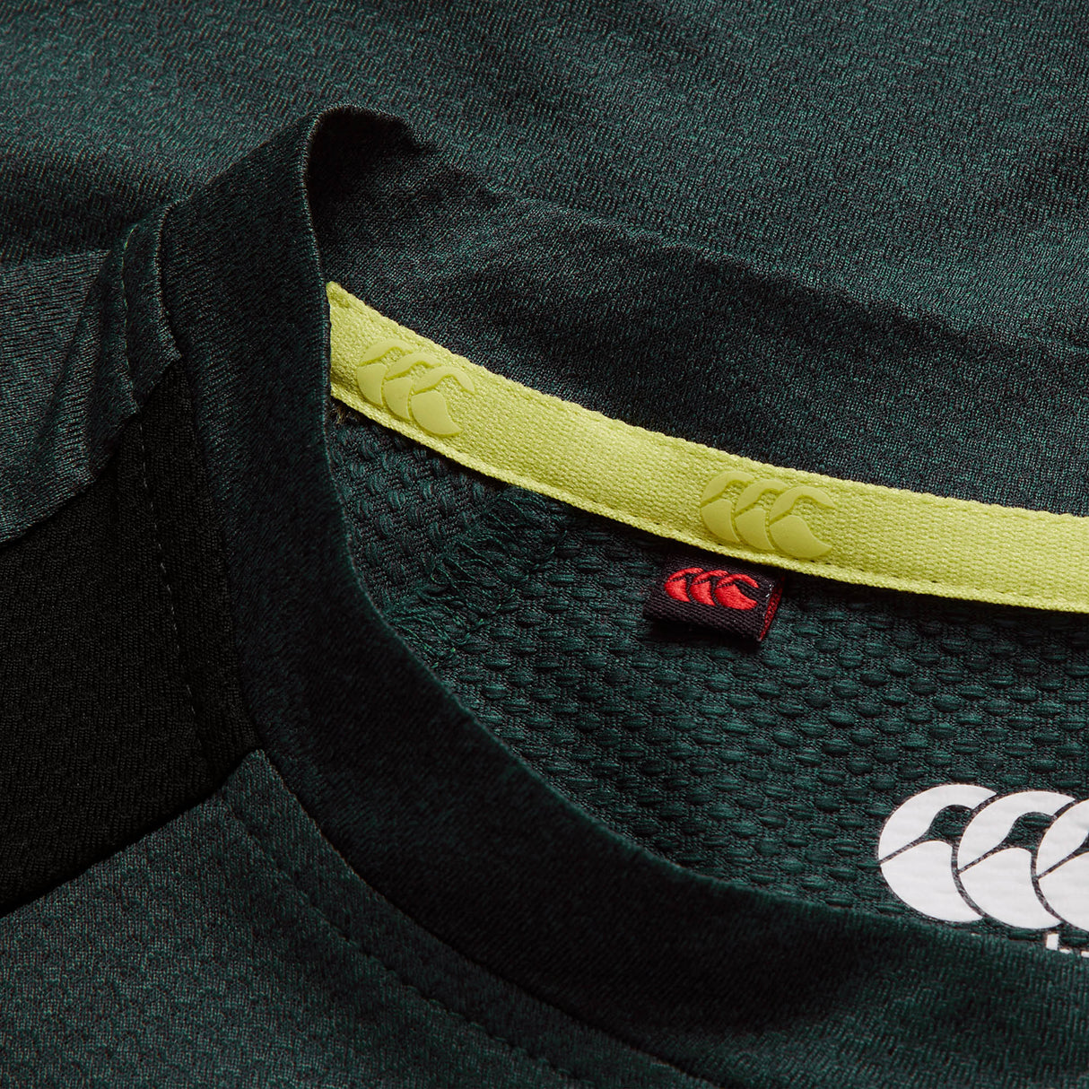 Close-up of the collar on the Canterbury Ireland 26 Elite Training Tee in dark green, featuring yellow trim and prominent white and red Canterbury logos inside and out, highlighting Vapodri breathable technology for optimal comfort.