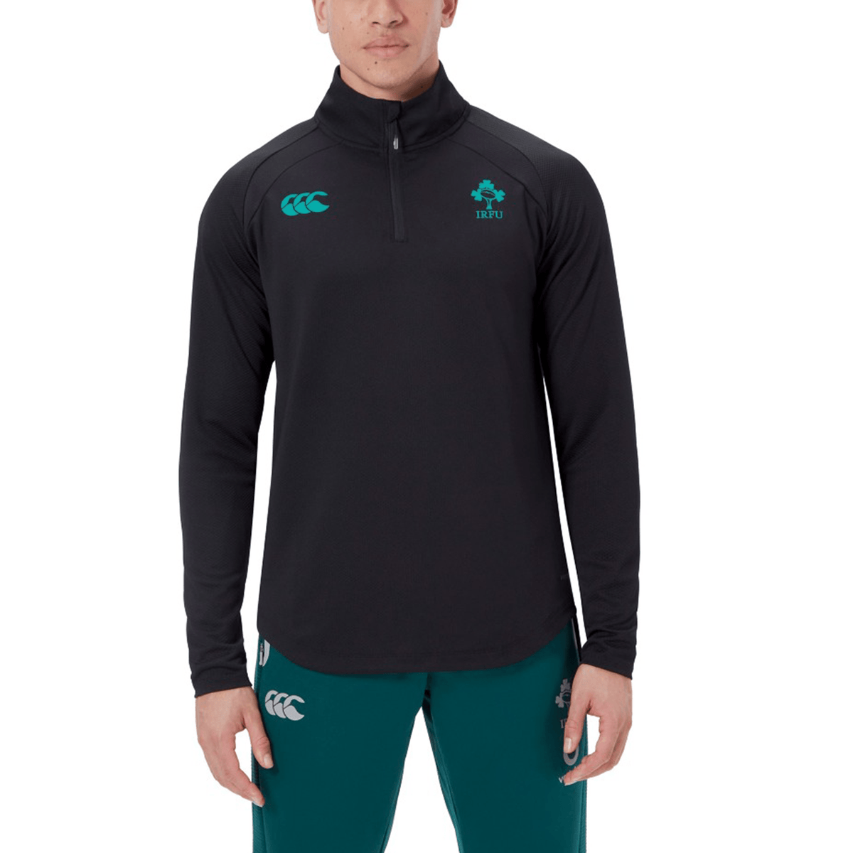 A person wearing the Canterbury Ireland 25 Elite First Layer training top in black with teal sports logos and matching teal athletic pants.