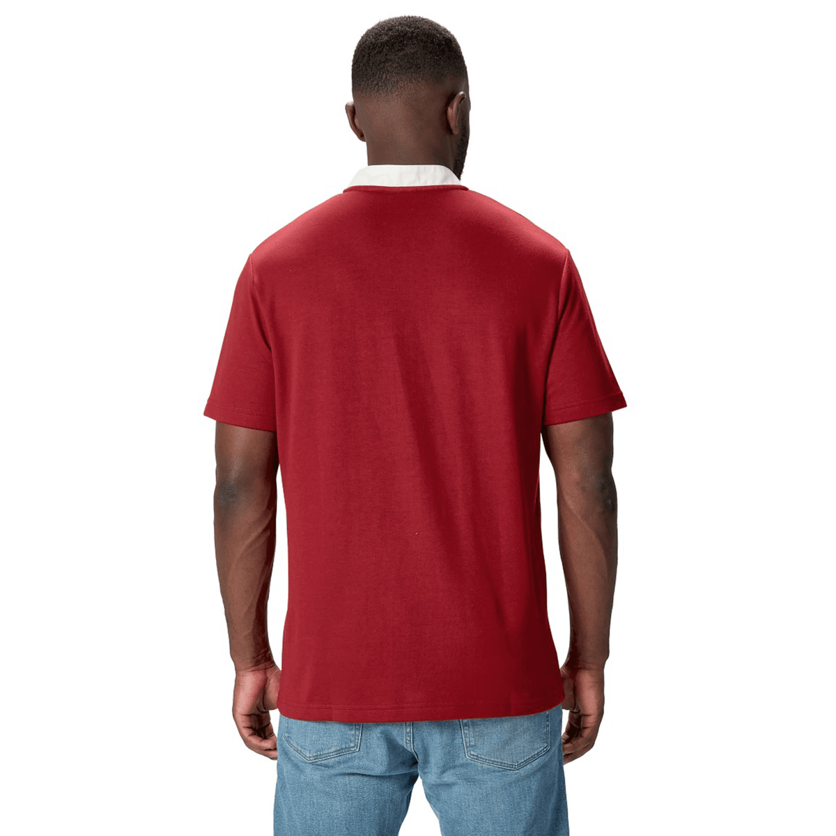 A person sporting the British & Irish Lions 2025 Classic Jersey by Canterbury, featuring a Red Dahlia color with a white collar, stands facing away, paired with blue jeans.