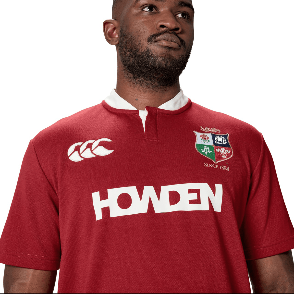 A person is wearing the British & Irish Lions 2025 Classic Jersey by Canterbury in red, featuring logos such as "Howden" and "Canterbury," as well as a "Since 1888" emblem.