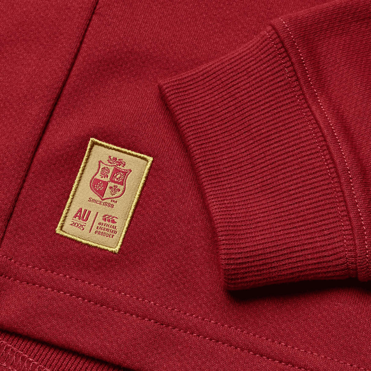 The Youth British & Irish Lions 2025 Long Sleeve Classic Jersey by Canterbury is maroon with a sewn beige patch featuring shields and text "Since 1829" and "AU 2025." Made from moisture-wicking fabric, it's ideal for active wearers.