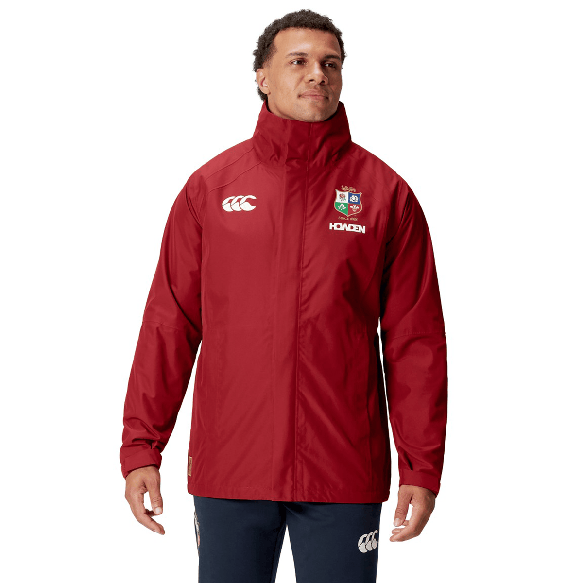 A person wearing a red British & Irish Lions 2025 Waterproof Jacket by Canterbury stands against a white background.