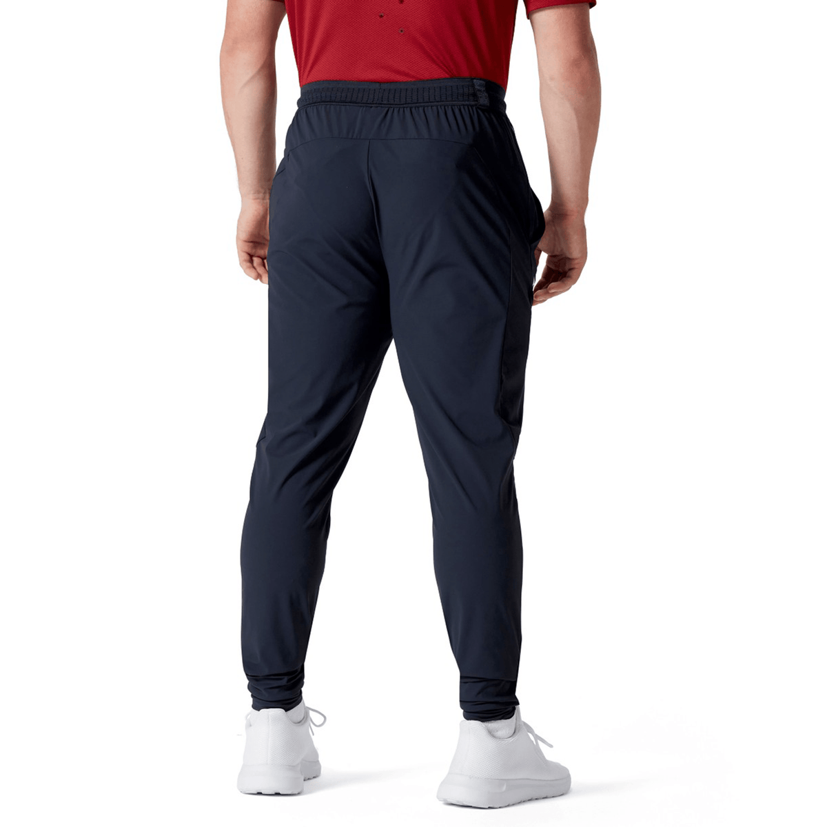 Individual in a red shirt, Canterbury's British & Irish Lions 2025 Everest Woven Pant, which is crafted from four-way stretch quick-drying fabric, and white sneakers, depicted from the back on a white background.